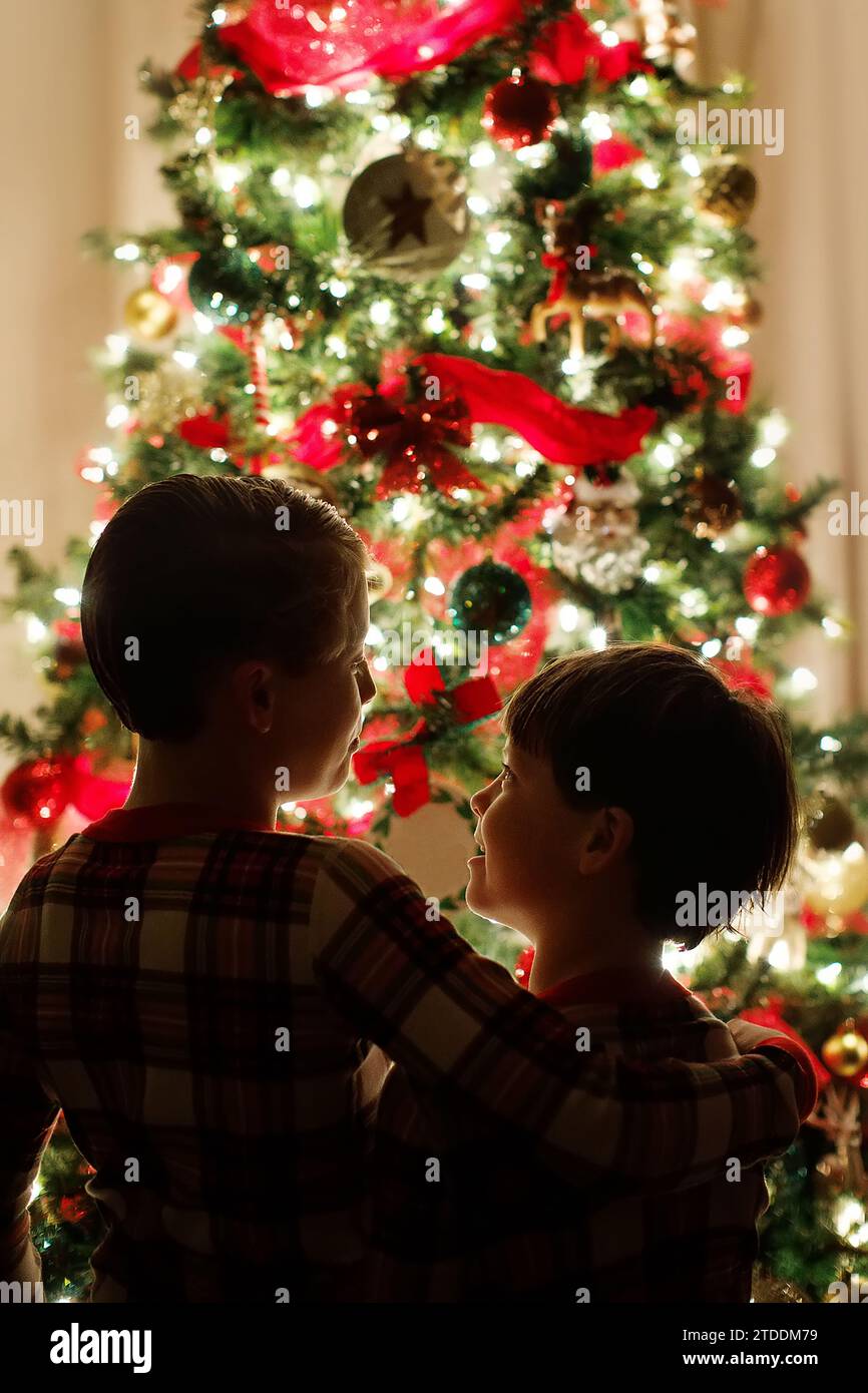 deux frères en pyjama serrés devant un sapin de noël illuminé Banque D'Images