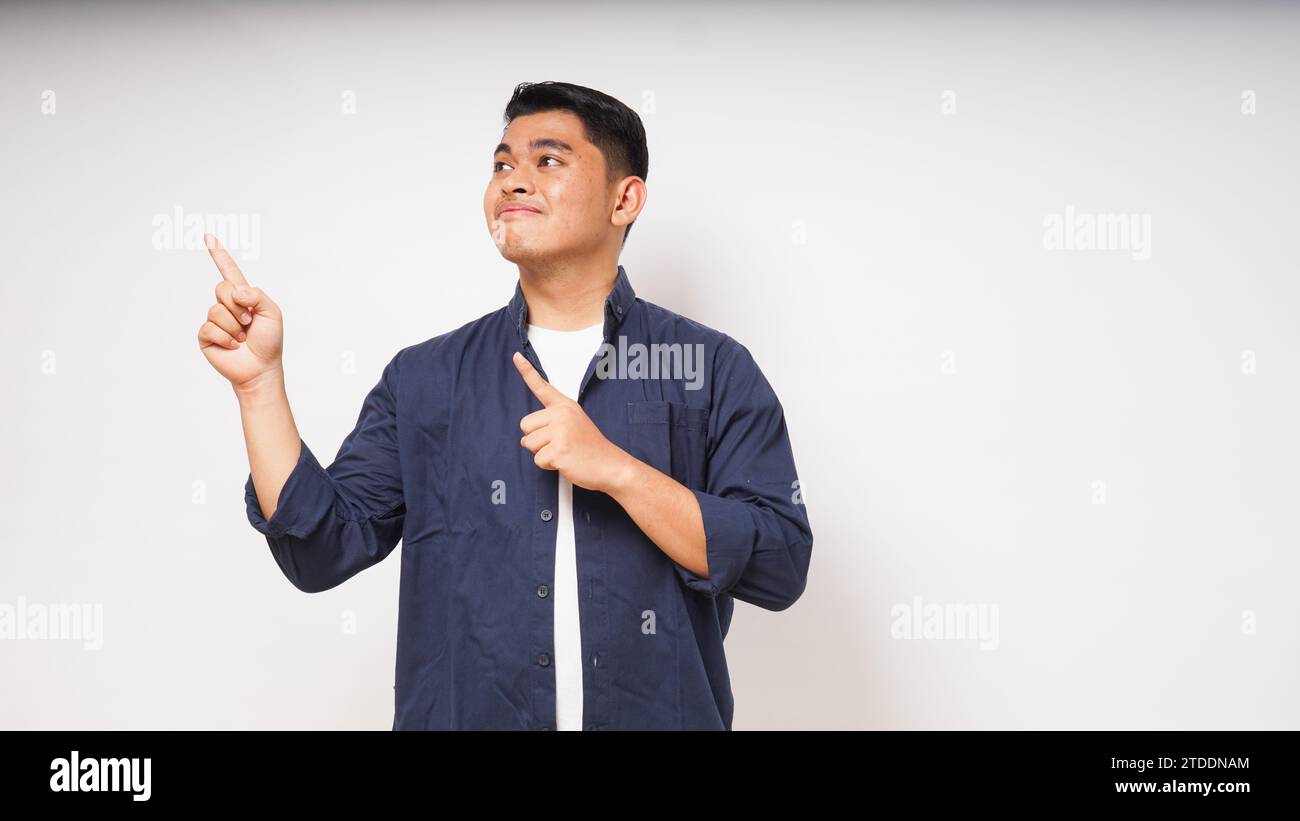 Jeune homme asiatique souriant en regardant et en pointant vers le côté droit sur fond blanc. prise de vue en studio Banque D'Images