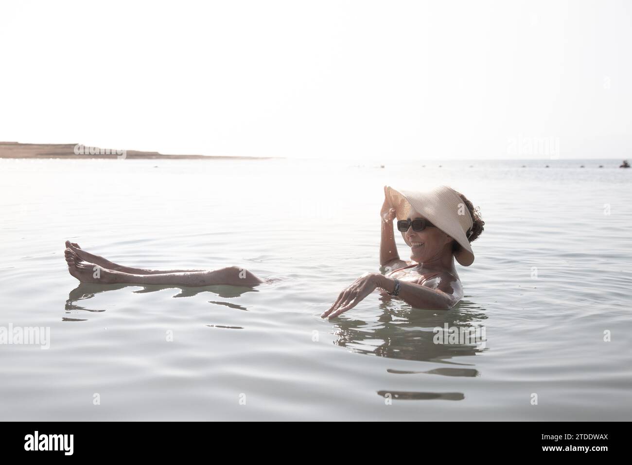 Femme portant un chapeau et des lunettes de soleil, flottant dans la mer Morte Banque D'Images