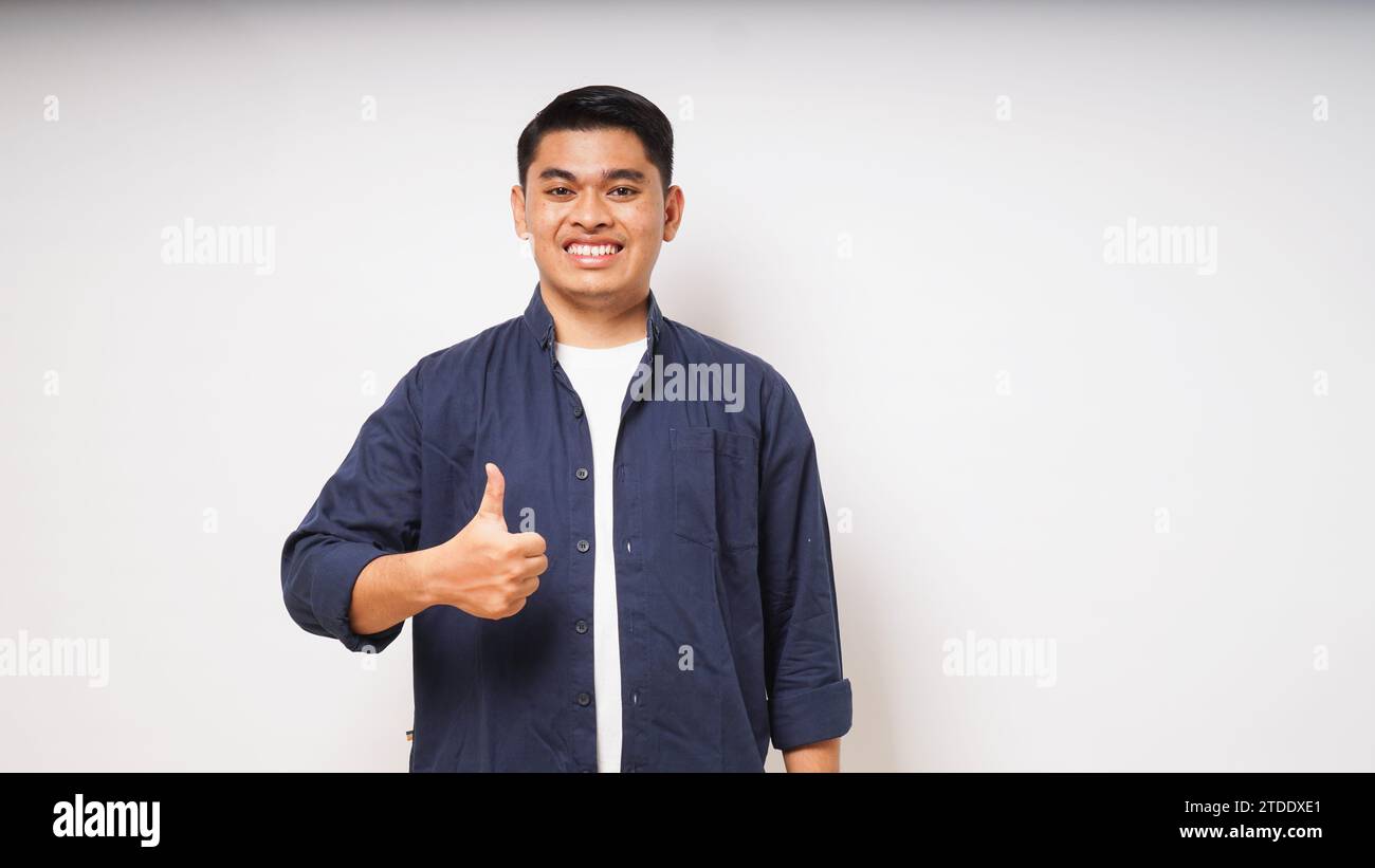 Jeune homme asiatique souriant et donnant le pouce à la caméra sur fond blanc. prise de vue en studio Banque D'Images