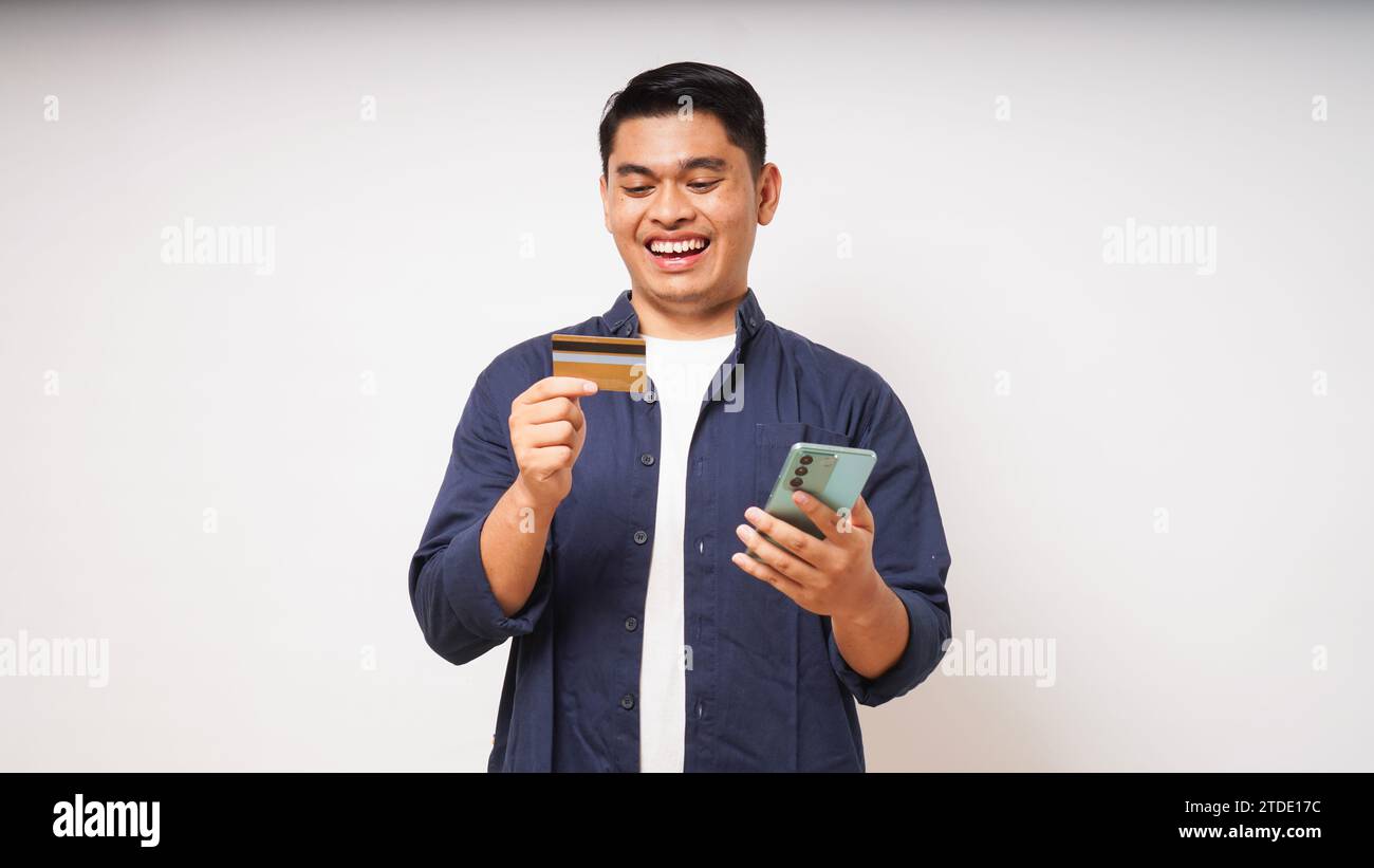 Portrait de heureux heureux heureux jeune homme asiatique tenant le téléphone intelligent et la carte de crédit, la saisie de données, les achats en ligne, le port de chemise décontractée. Studio intérieur s Banque D'Images