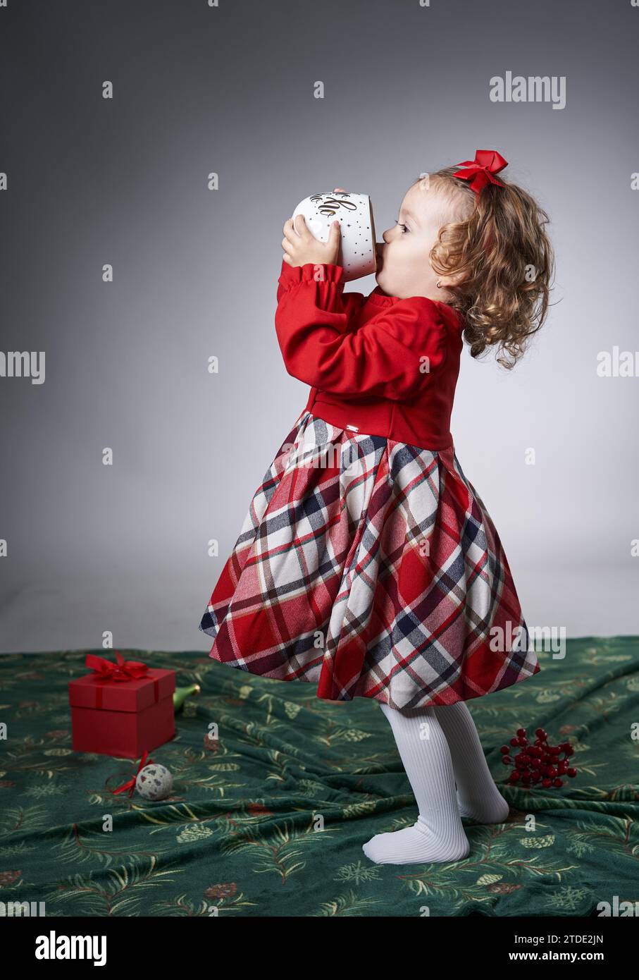 Portrait d'une adorable petite fille blonde aux cheveux bouclés avec une énorme tasse à lait pour Noël, sur fond gris, photo studio Banque D'Images