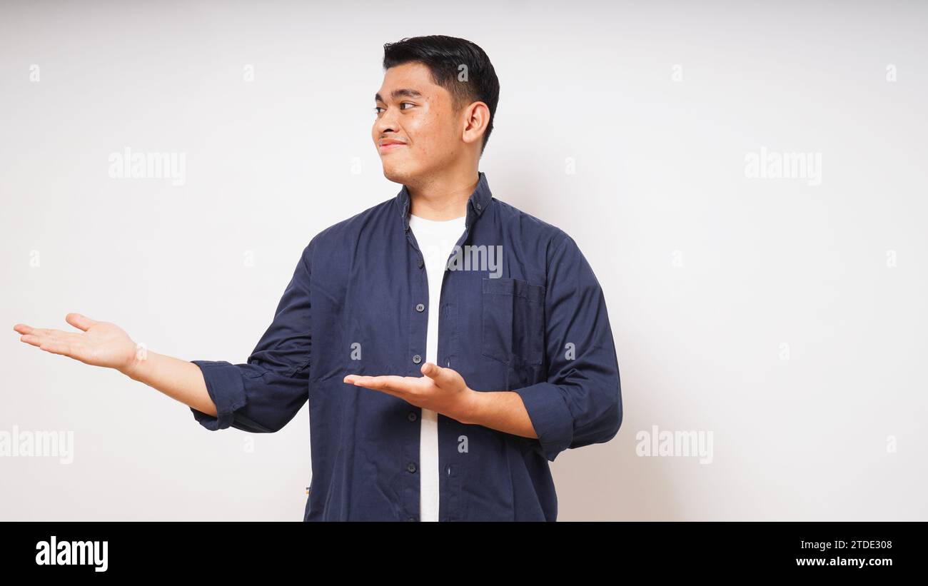 Jeune homme asiatique souriant en regardant et en pointant vers le côté droit sur fond blanc. prise de vue en studio Banque D'Images