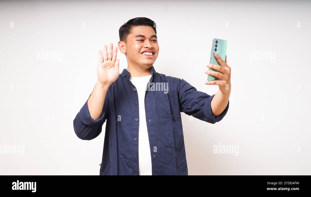 Homme asiatique montrant l'expression heureuse en agitant la main pendant l'appel vidéo sur fond blanc. prise de vue en studio Banque D'Images