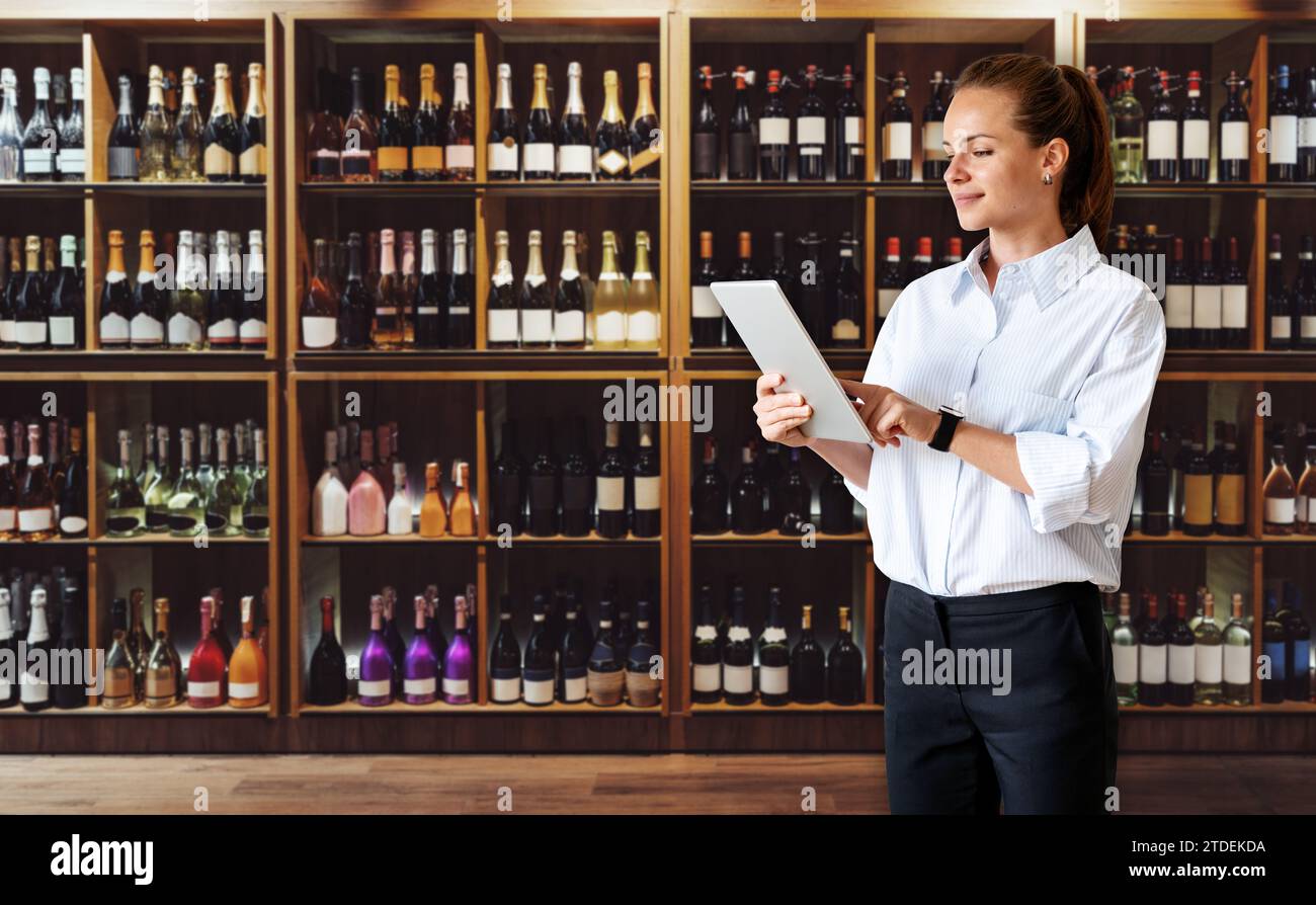 Gestionnaire de femme d'affaires avec tablette numérique en main debout dans la surface de vente du magasin d'alcool. Magasin de vin d'affaires. Banque D'Images