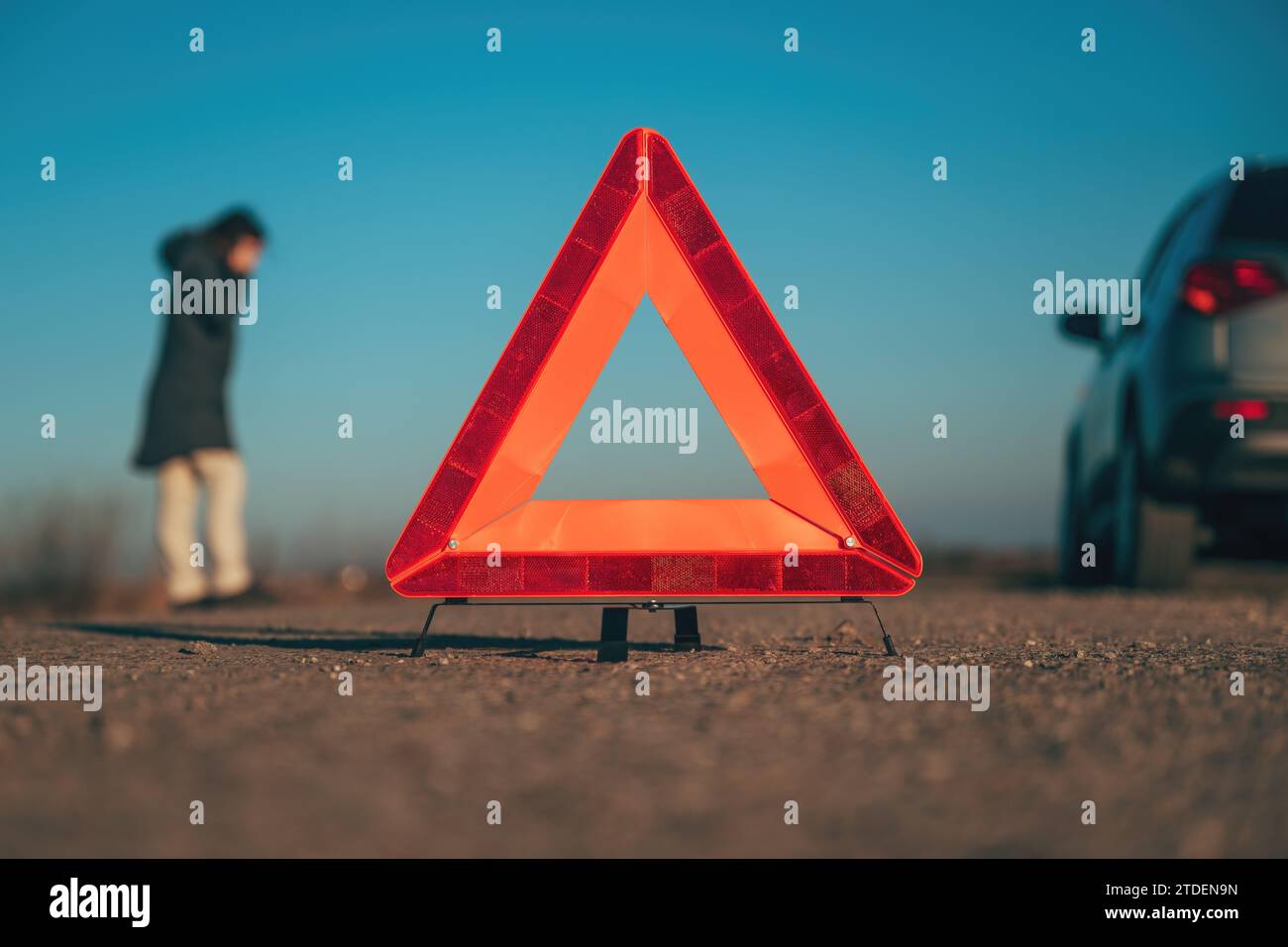 Panne de véhicule, triangle d'avertissement rouge sur la route avec une voiture en panne et une femme faisant un appel téléphonique au service routier, mise au point sélective Banque D'Images