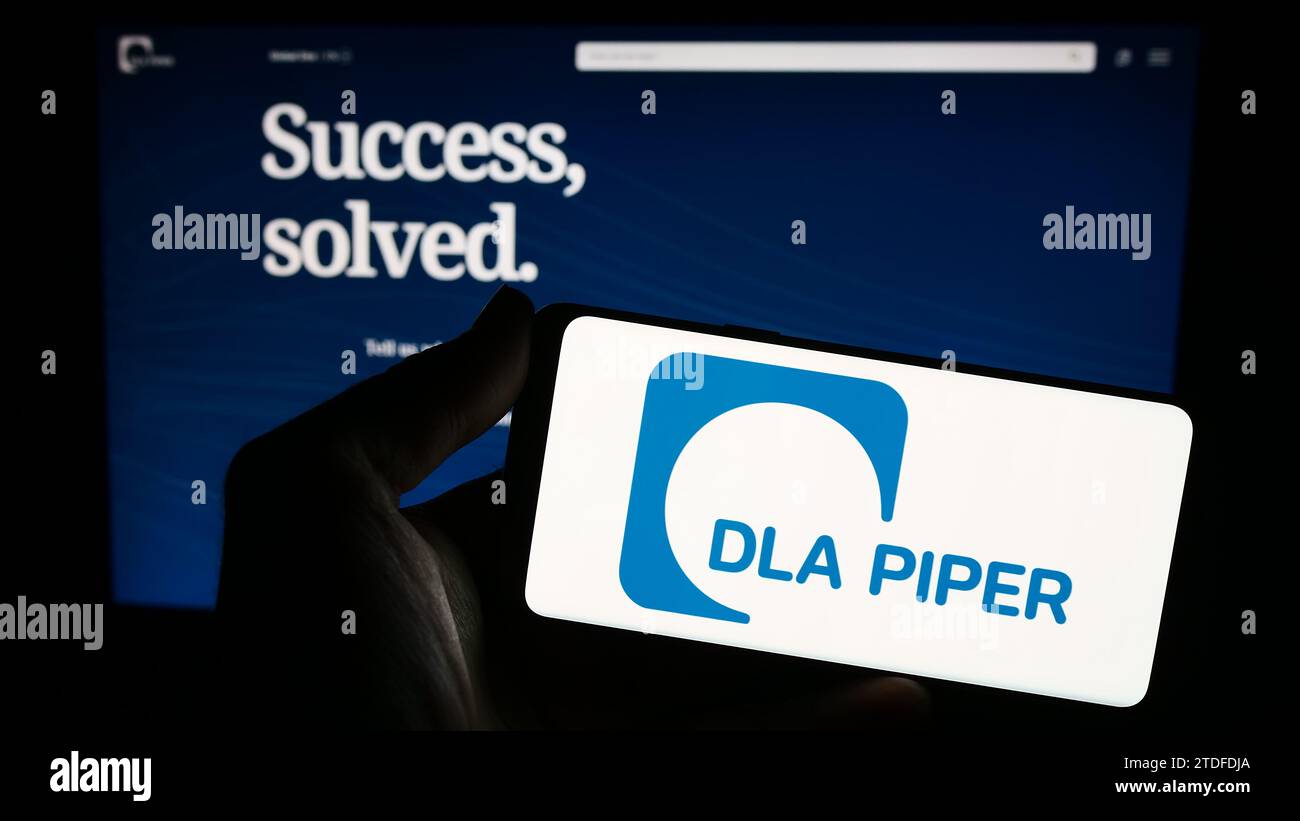 Personne tenant le smartphone avec le logo du cabinet d'avocats DLA Piper devant le site Web. Concentrez-vous sur l'affichage du téléphone. Banque D'Images