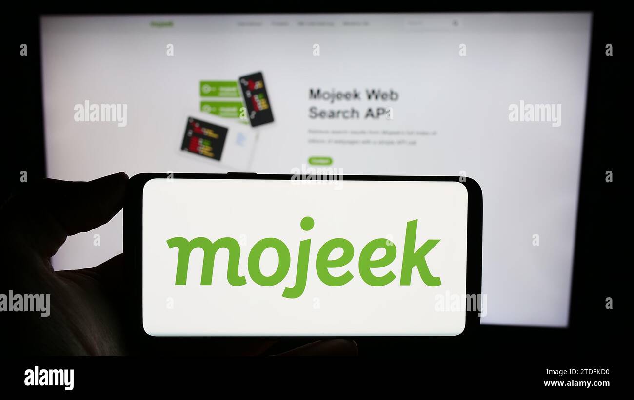 Personne tenant le téléphone portable avec le logo de la société britannique de moteur de recherche en ligne Mojeek en face de la page Web d'affaires. Concentrez-vous sur l'affichage du téléphone. Banque D'Images