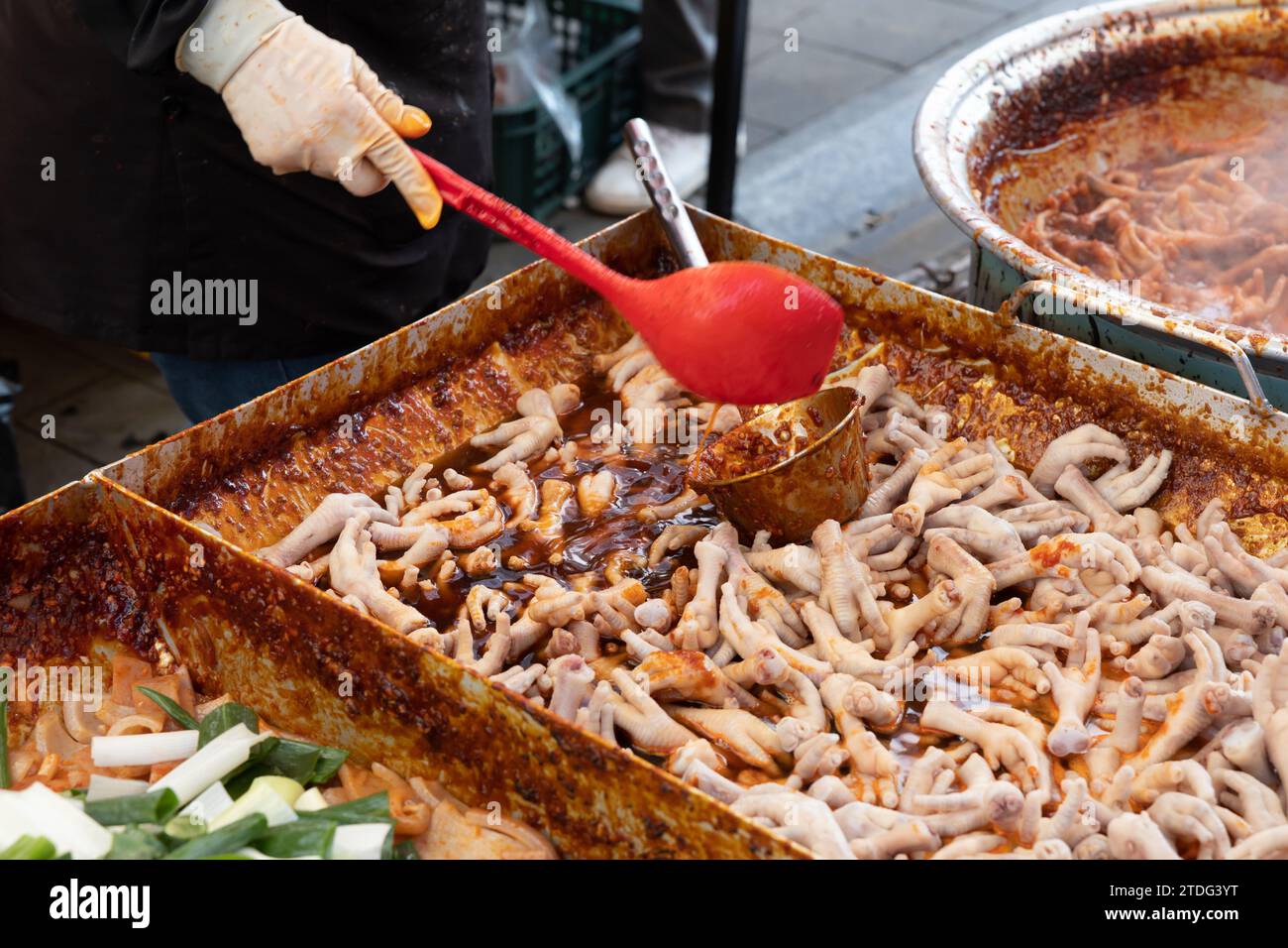 Pieds de poulet sautés à vendre sur un marché traditionnel en Corée et cuisine à la main d'un marchand avec une louche Banque D'Images