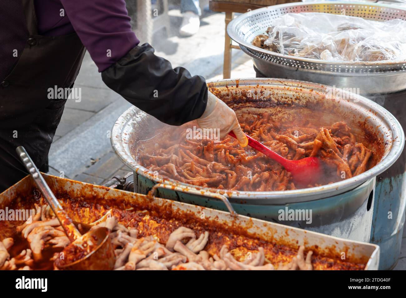 Pieds de poulet sautés à vendre sur un marché traditionnel en Corée et cuisine à la main d'un marchand avec une louche Banque D'Images