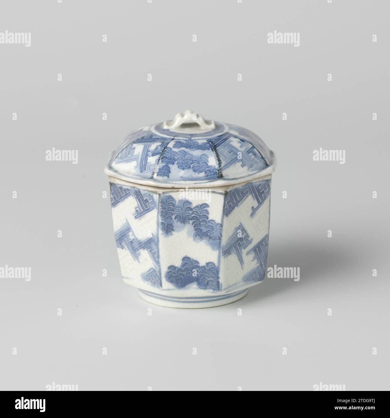 Pot couvert octogonal avec des plantes, des paquets de bambou et des bordures ornementales, anonyme, c. 1690 - c. 1700 couvercle octogonal pot de porcelaine, peint en bleu sous glaçure. Sur le mur deux compartiments avec des paquets de bambou, deux avec des plantes et quatre avec un motif de swastika en relief. Le couvercle avec la même décoration avec une bande avec un motif de méandre autour du bouton. Glaçage craquelé. Bleu blanc. Porcelaine du Japon. glaçage. Cobalt (minéral) peinture / vitrification couvercle octogonal pot de porcelaine, peint en bleu sous glaçure. Sur le mur deux compartiments avec des paquets de bambou, deux avec des plantes et fo Banque D'Images