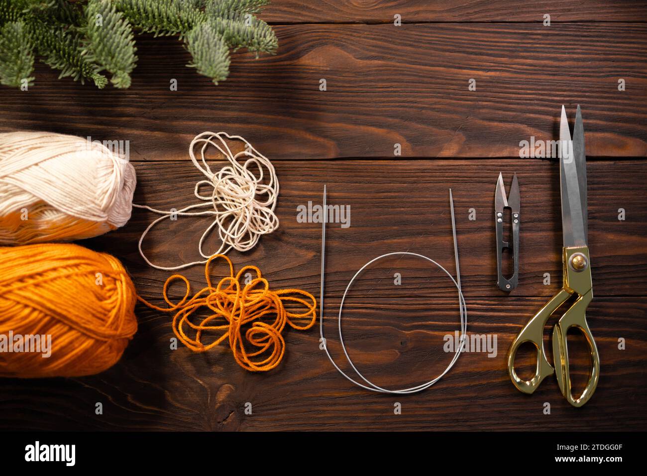 ciseaux, aiguilles à tricoter et fils sur une table en bois décorée de branches de sapin Banque D'Images
