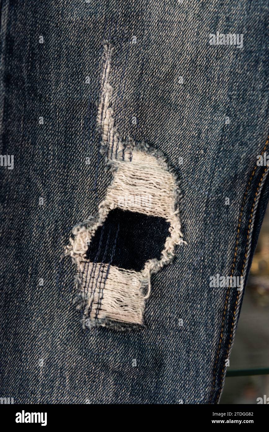 Gros plan d'un pantalon jean jean bleu déchiré, déchiré et effiloché détail de jambe avec des trous et des fils lâches. Banque D'Images
