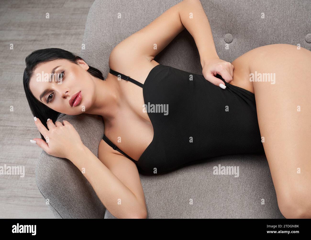 Femme pensive sexy en body, couchée sur un canapé gris, regardant la caméra. Vue de dessus du magnifique modèle femme caucasienne en maillot de bain reposant sur le canapé i. Banque D'Images Femme pensive sexy en body, couchée sur un canapé gris, regardant la caméra. Vue de dessus du magnifique modèle femme caucasienne en maillot de bain reposant sur le canapé i. Banque D'Images