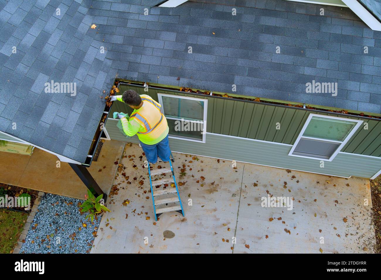 Ce travailleur nettoie les drains de gouttière de toit bouchés qui sont devenus obstrués par la saleté, les débris, les feuilles tombées Banque D'Images