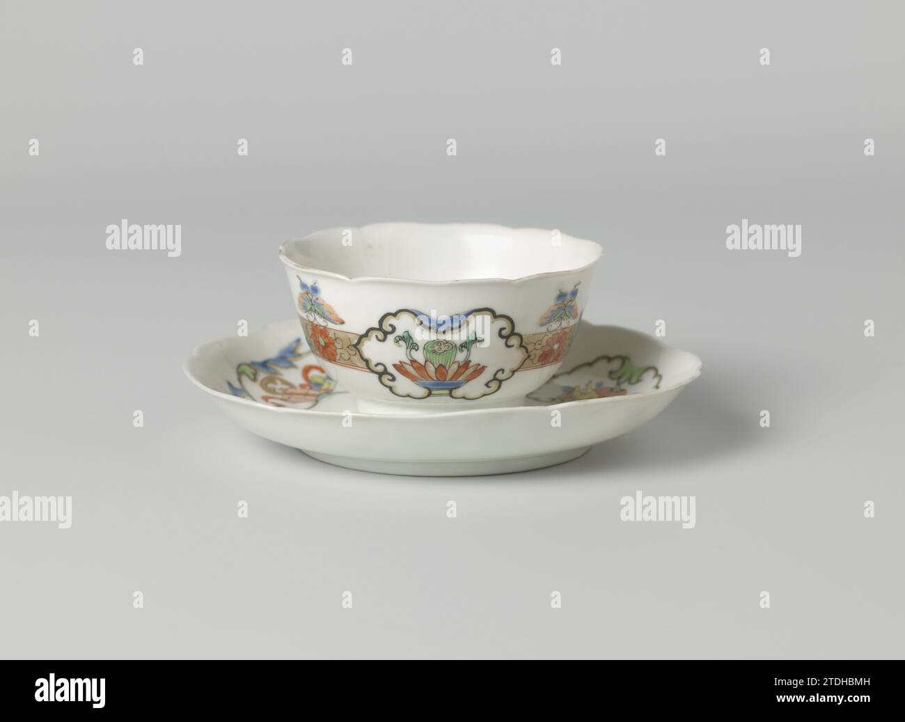 Tasse et soucoupe en forme de cloche avec papillons, rouleaux floraux et objets auspicieux en panneaux, anonyme, c. 1725 - c. 1749 tasse et soucoupe en forme de cloche en porcelaine avec mur lobé, peintes sur la glaçure en bleu, rouge, vert, jaune, noir et or. Sur le plat du plat au centre une rosette de vignes de fleurs stylisées ; autour de cela une bande de vignes de fleurs et de papillons entrecoupés de trois cartouches avec des symboles chanceux : corbeille de fruits (fingercitroen, pêche), fleur de lotus avec gousse ou livres et rouleaux. La tête avec la même décoration. Une fissure dans le mur de la tête. Famle Rose. China porcel Banque D'Images