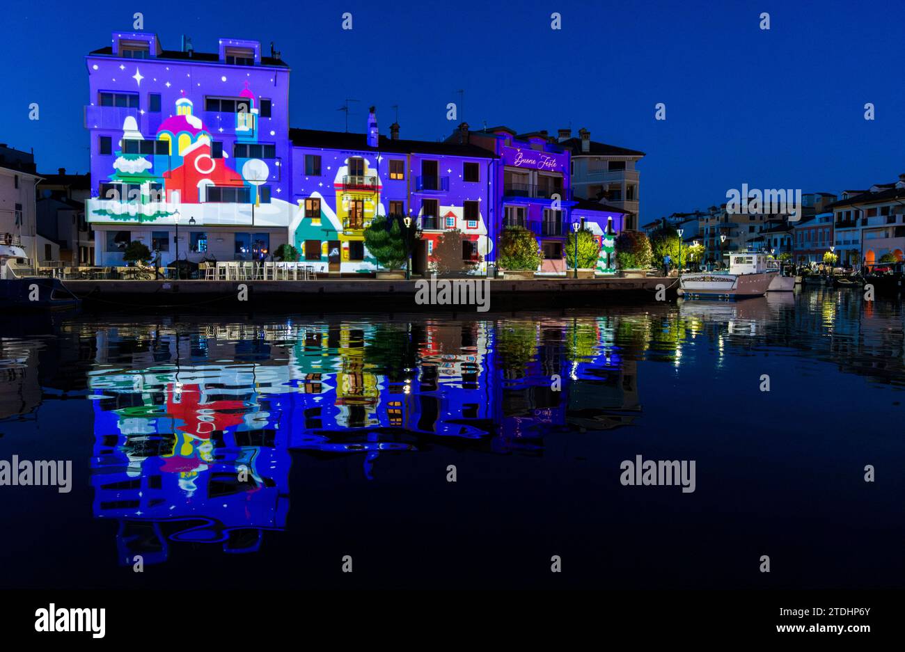 Grado, Italie - 10 décembre 2023 : vue depuis le port de Mandracchio des lumières de Noël colorées projetées sur les bâtiments et les maisons. Holographique 3D. Banque D'Images