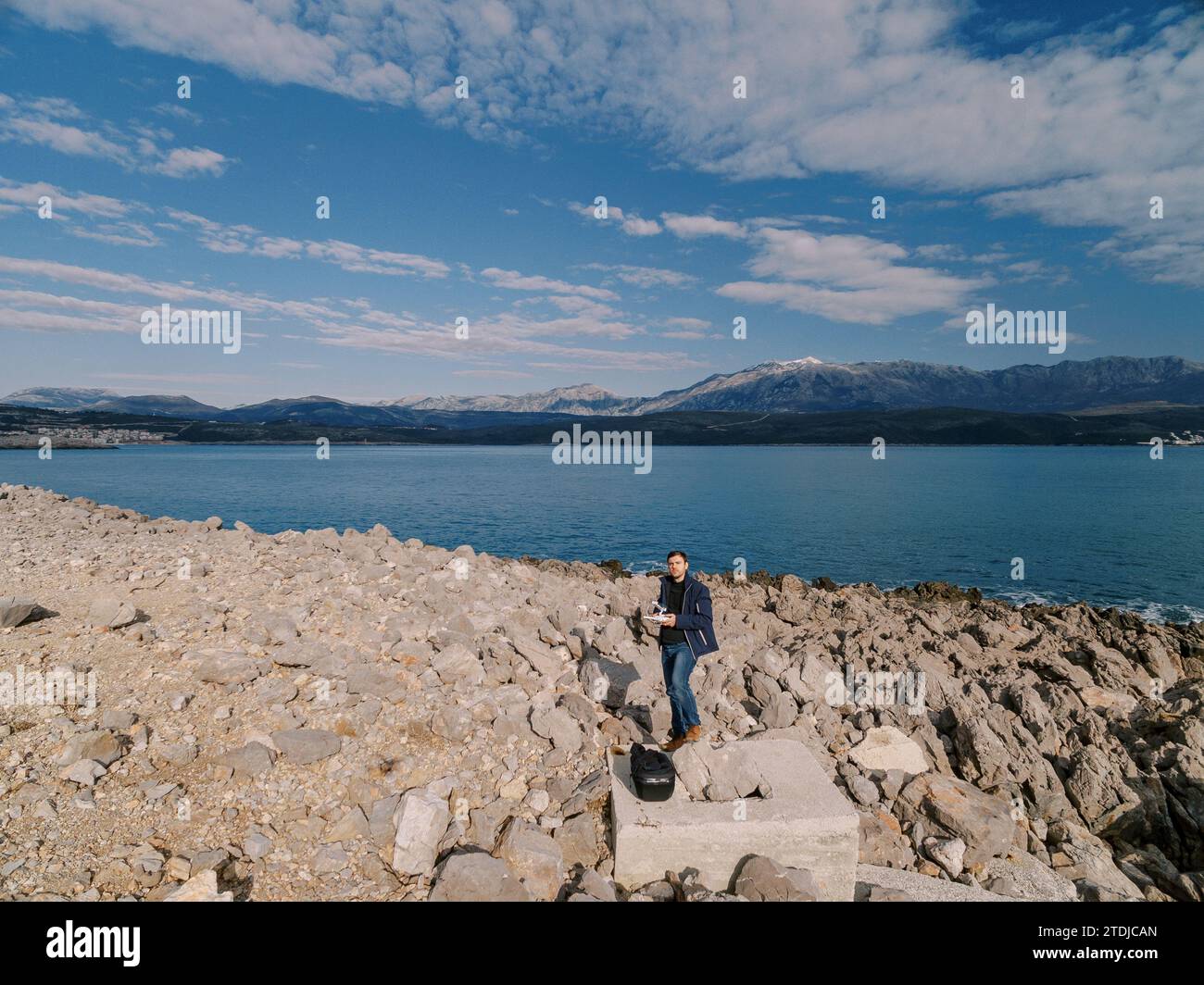 Opérateur avec une télécommande de drone dans ses mains se tient sur une plate-forme en pierre sur un bord de mer rocheux Banque D'Images
