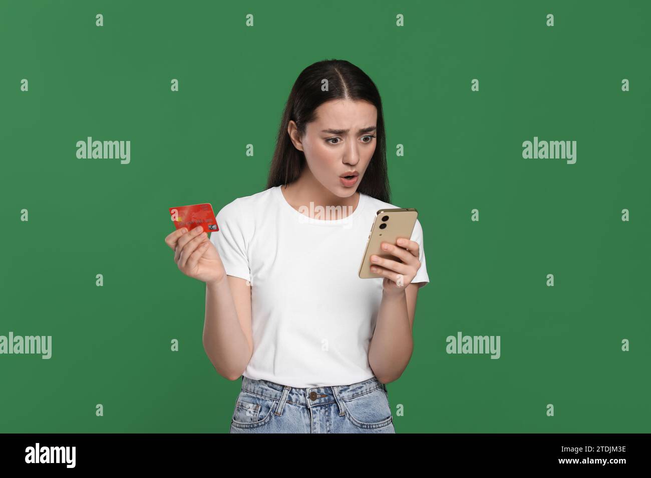 Femme choquée avec carte de crédit et smartphone sur fond vert. Problème de dette Banque D'Images