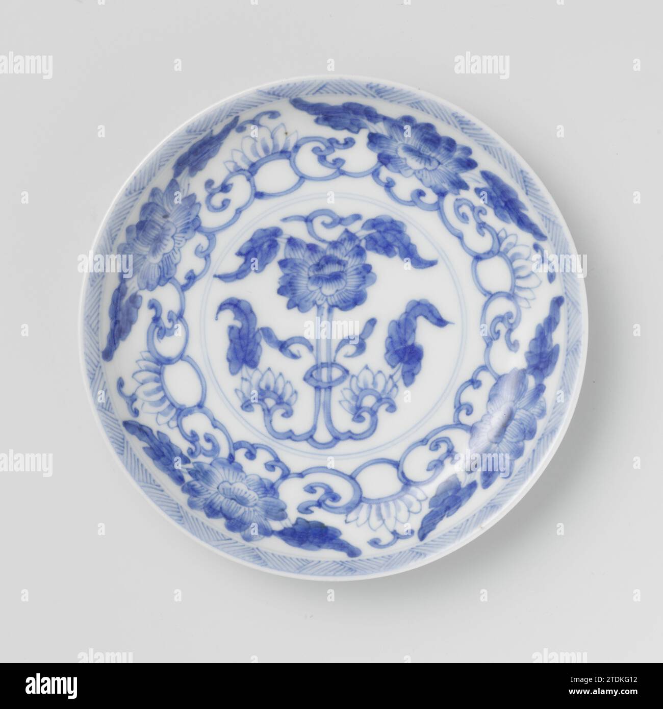 Soucoupe avec des rouleaux de lotus et des champignons, anonyme, c. 1700 - c. 1724 plat avec un mur rond de porcelaine, peint en bleu sous glaçage. Sur le plat un lotus stylisé et la pivoine boivent dans un médaillon ; sur le médaillon un motif relié de lotus et de pivoine boivent ; le bord avec un motif en zigzag ; l'arrière avec quatre fois un champignon (Lingzhi). Marqué sur le fond avec le caractère de la marque 'Yù', Jade, dans un double cercle. Bleu blanc. Porcelaine de Chine. glaçage. Plat de peinture / vitrification au cobalt (minéral) avec un mur rond de porcelaine, peint en bleu sous glaçage. Sur le plat un lotus stylisé et pivoine d Banque D'Images