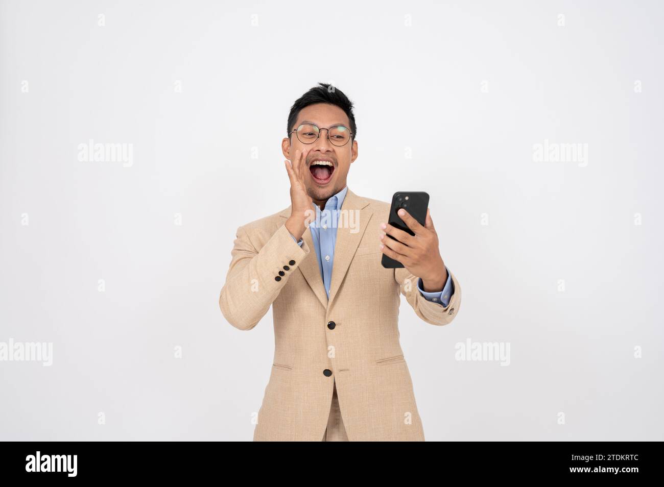 Un homme d'affaires asiatique choqué et excité regarde l'écran de son téléphone avec un visage surprenant tout en se tenant debout sur un fond blanc isolé. offre spéciale Banque D'Images