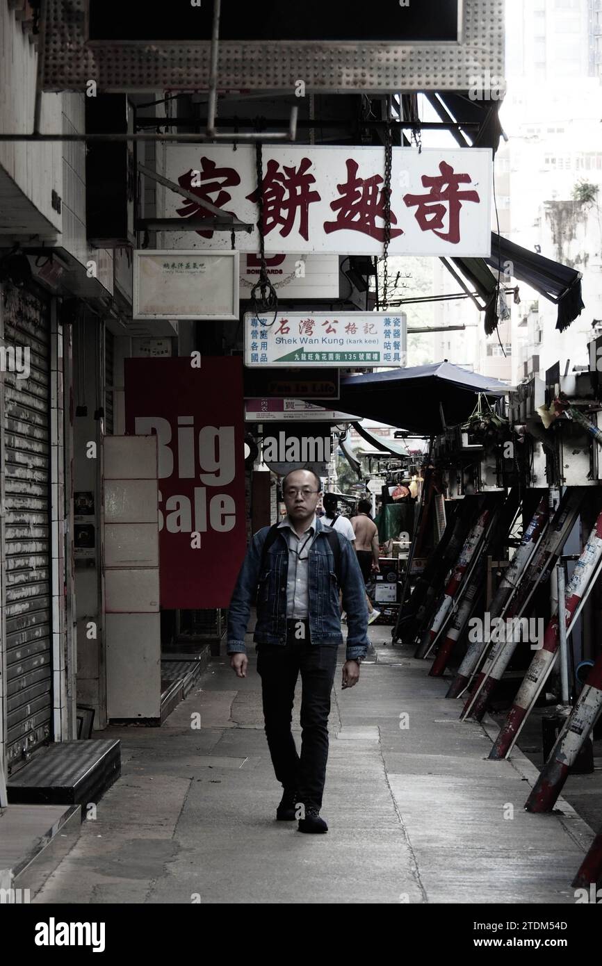 Un homme marchant dans une rue de Hong Kong sous la signalisation d'une célèbre pâtisserie, allant travailler un matin calme habituel Banque D'Images