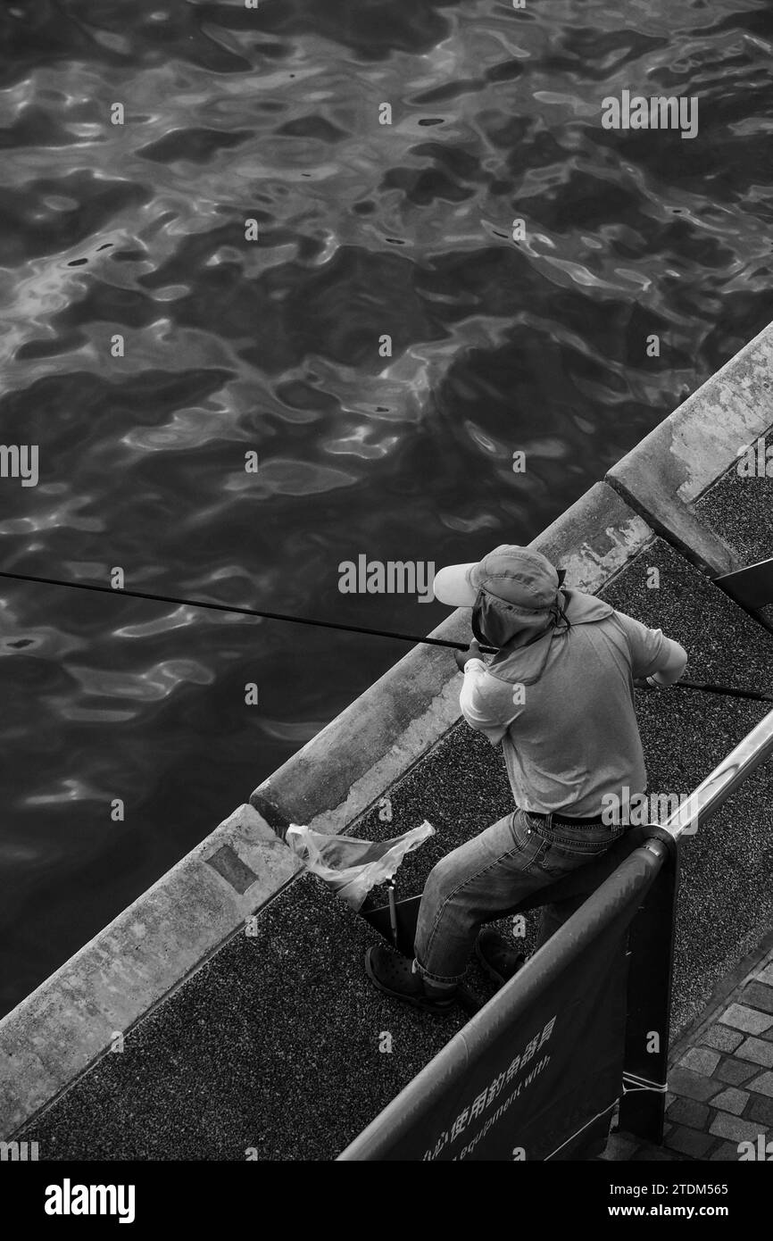 Un homme vu pêcher près du port Victoria à Hong Kong Banque D'Images