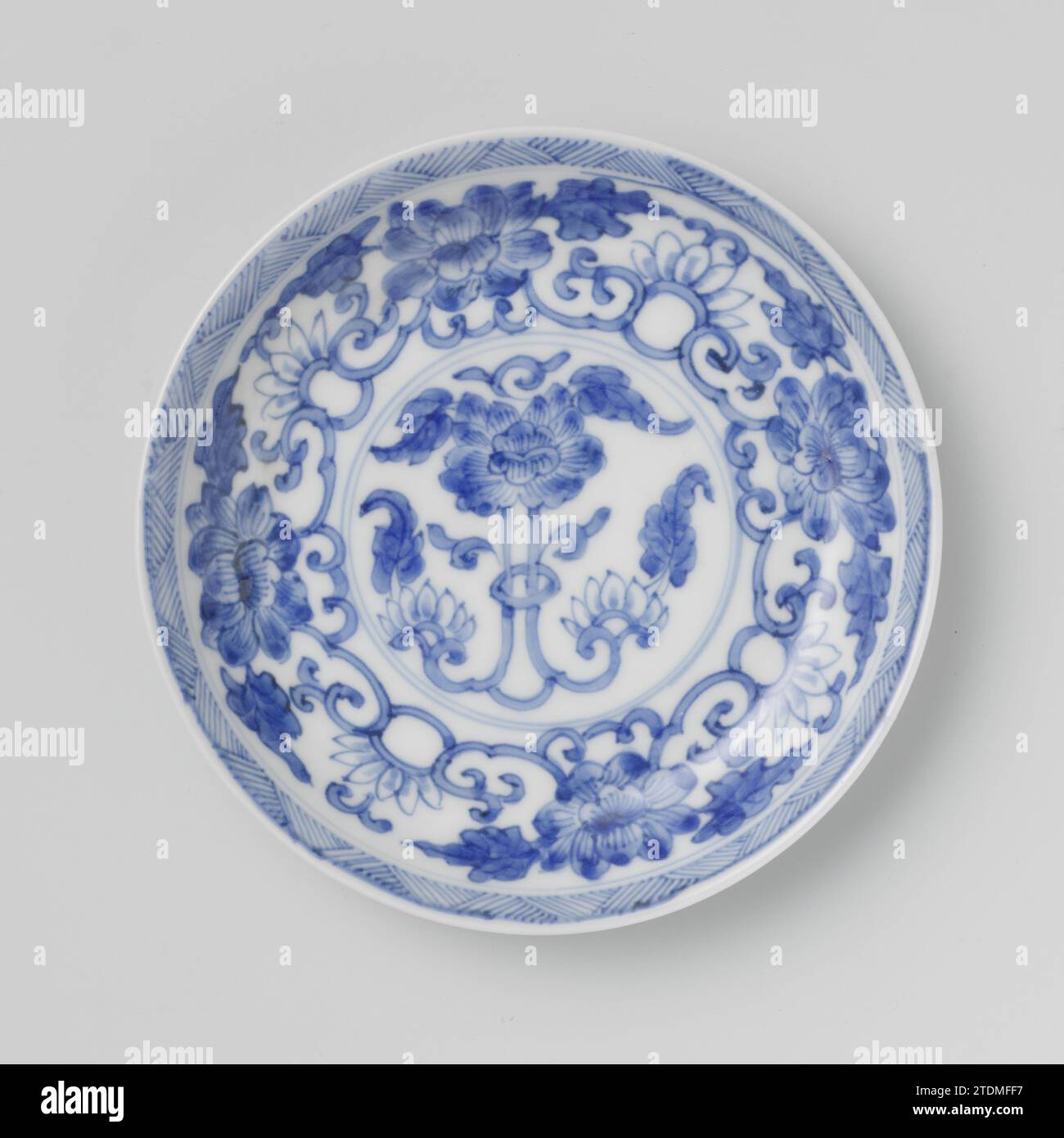 Soucoupe avec des rouleaux de lotus et des champignons, anonyme, c. 1700 - c. 1724 plat avec un mur rond de porcelaine, peint en bleu sous glaçage. Sur le plat un lotus stylisé et la pivoine boivent dans un médaillon ; sur le médaillon un motif relié de lotus et de pivoine boivent ; le bord avec un motif en zigzag ; l'arrière avec quatre fois un champignon (Lingzhi). Marqué sur le fond avec le caractère de la marque 'Yù', Jade, dans un double cercle. Bleu blanc. Porcelaine de Chine. glaçage. Plat de peinture / vitrification au cobalt (minéral) avec un mur rond de porcelaine, peint en bleu sous glaçage. Sur le plat un lotus stylisé et pivoine d Banque D'Images