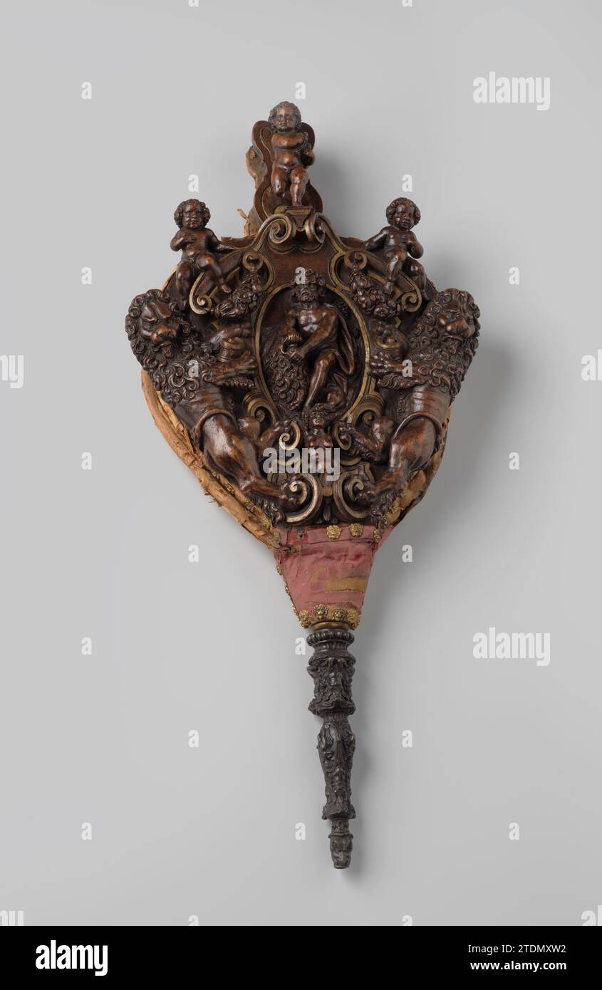 Bladderbalg de noyer partiellement doré avec Samson, entre autres, qui brise le Muil du Lion, Anonyme, 1550 - 1600 Bladderball fait de noyer partiellement doré. Le sommet sculpté en relief montre deux lions qui tiennent un cartouche de travail à rouleaux avec Simson qui brise la bouche du lion ; en dessous une figure féminine, se terminant par le bas par des volutes de feuilles. Il y a deux putti sur les travaux de roulement sur le dessus ; sur la poignée un putto avec oiseau. Le velours rouge de la feuille arrière est cloué avec des clous en cuivre doré avec des masques de lion. Le chalumeau articulé montre diverses figures et masques. Italie bois (matériel végétal). Banque D'Images