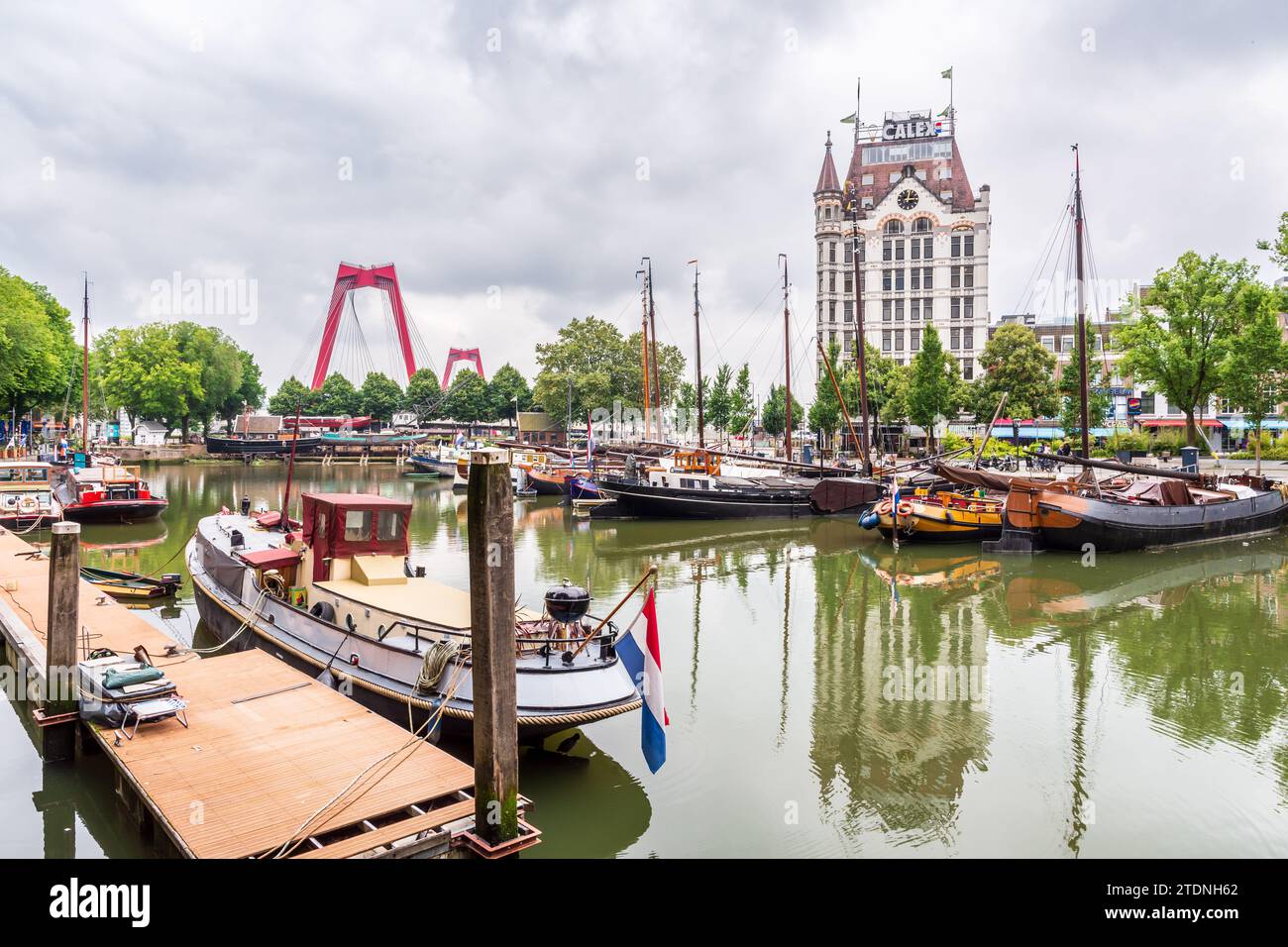 Le vieux port de Rotterdam avec des bateaux fluviaux, surplombé par le bâtiment historique Witte huis et les pylônes rouges du Willemsbrug, sous un ciel orageux. Banque D'Images