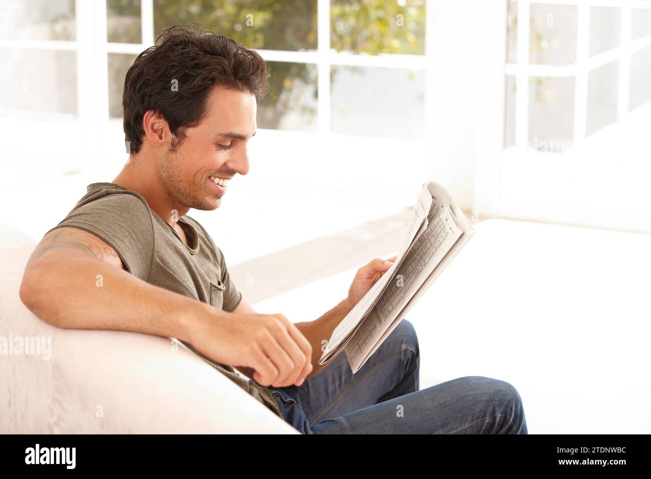 Homme, lecture et heureux avec journal sur le canapé pour se détendre, pause du matin et informations dans le salon. Personne, visage et sourire pour article, histoire et Banque D'Images