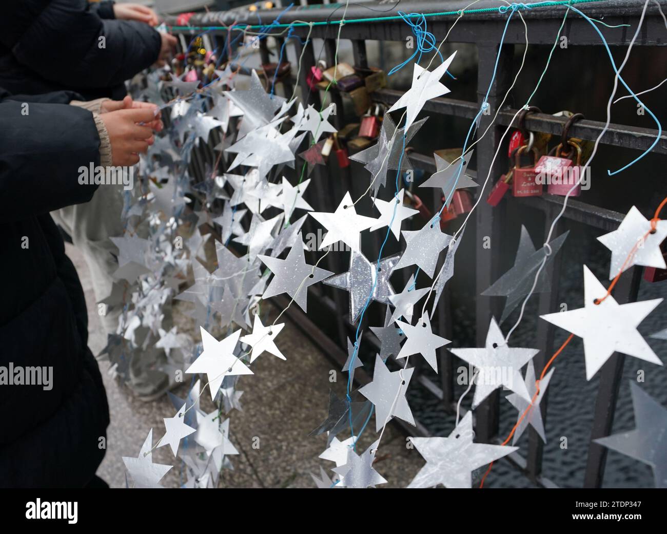 Hambourg, Allemagne. 19 décembre 2023. Les écolières attachent des étoiles faites maison faites à partir des couvercles en aluminium de yogourt et de tasses à pudding au pont Michaelis dans le centre-ville. Dans la tentative de record du monde, les élèves veulent illuminer le pont Michaelis avec 18 800 étoiles auto-fabriquées sur des lumières de fée. Les recettes de la campagne iront à l'hospice pour enfants de Sternenbrücke. Crédit : Marcus Brandt/dpa/Alamy Live News Banque D'Images