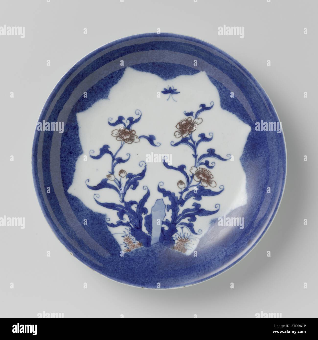 Soucoupe-plat avec poudre bleue et panneau façonné en réserve avec sprays de fleurs, anonyme, c. 1700 - c. 1724 plat avec un mur rond de porcelaine, peint dans le glaçage sous-jacent bleu et rouge. Le plat est recouvert de poudré bleu (bleu poudré) avec un cartouche en forme de fleur rempli de rochers, de branches de fleurs et d'un papillon sur le plat en elle ; trois vignes de fleurs à l'extérieur. Marqué sur le dessous avec la marque à six personnages de Keizer Chenghua. Quelques éclats et deux fissures dans le bord. Sous-glacer bleu avec rouge cuivre. Porcelaine de Chine. glaçage. cobalt (minéral). Peinture sur cuivre (métal) / vitrification Di Banque D'Images