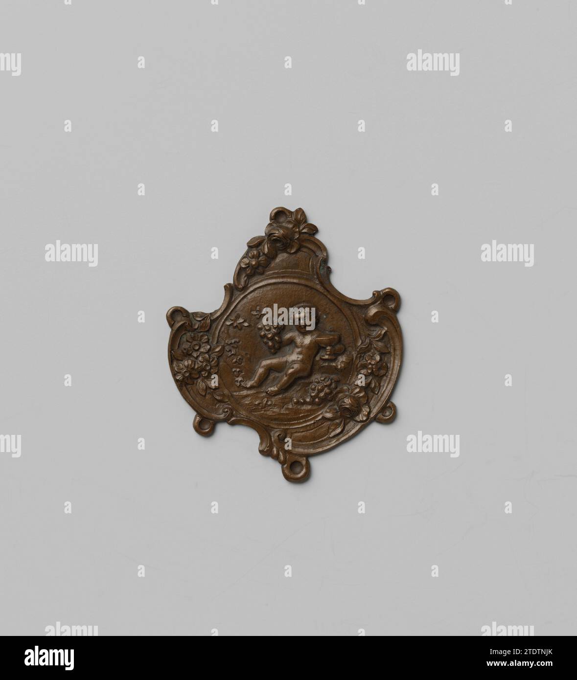 Modèle pour un élément décoratif d'une chatelaine, anonyme, c. 1750 - c. 1775 le modèle chassé hors de la plaque pour un moule est équipé d'un médaillon entouré d'ornement rococo avec un putto avec des vros de raisin et calice. Six yeux le long des bords pour attacher les liens. Amsterdam cuivre (métal) le modèle chassé de la plaque pour un moule est équipé d'un médaillon entouré d'ornement rococo avec un putto avec des vros de raisin et calice. Six yeux le long des bords pour attacher les liens. Cuivre Amsterdam (métal) Banque D'Images