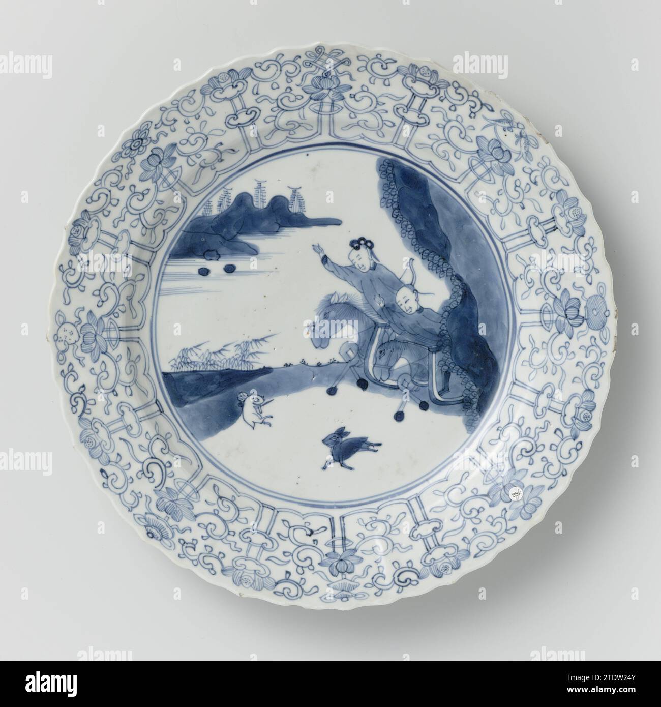 Soucoupe-plat avec scène de chasse, rouleaux de lotus et symboles auspicieux, anonyme, c. 1700 - c. 1724 soucoupe en porcelaine avec mur rond, côtelé et bord festonné, peinte en bleu sous-laque. Sur le plat une scène de chasse avec deux cavaliers armés dans un paysage, la chasse d'un lièvre ; le bord avec une bande connectée de Lotusranken, entre lesquels les huit symboles chanceux (chakra, coquille, parasol, baldaquin, lotus, vase, pêche, noeud infini) ; le dos avec seize branches de fleurs lâches. Marqué sur le dessous avec la marque à six caractères de Keizer Chenghua dans un double cercle. Rand légèrement endommagé. Bleu blanc. Chi Banque D'Images