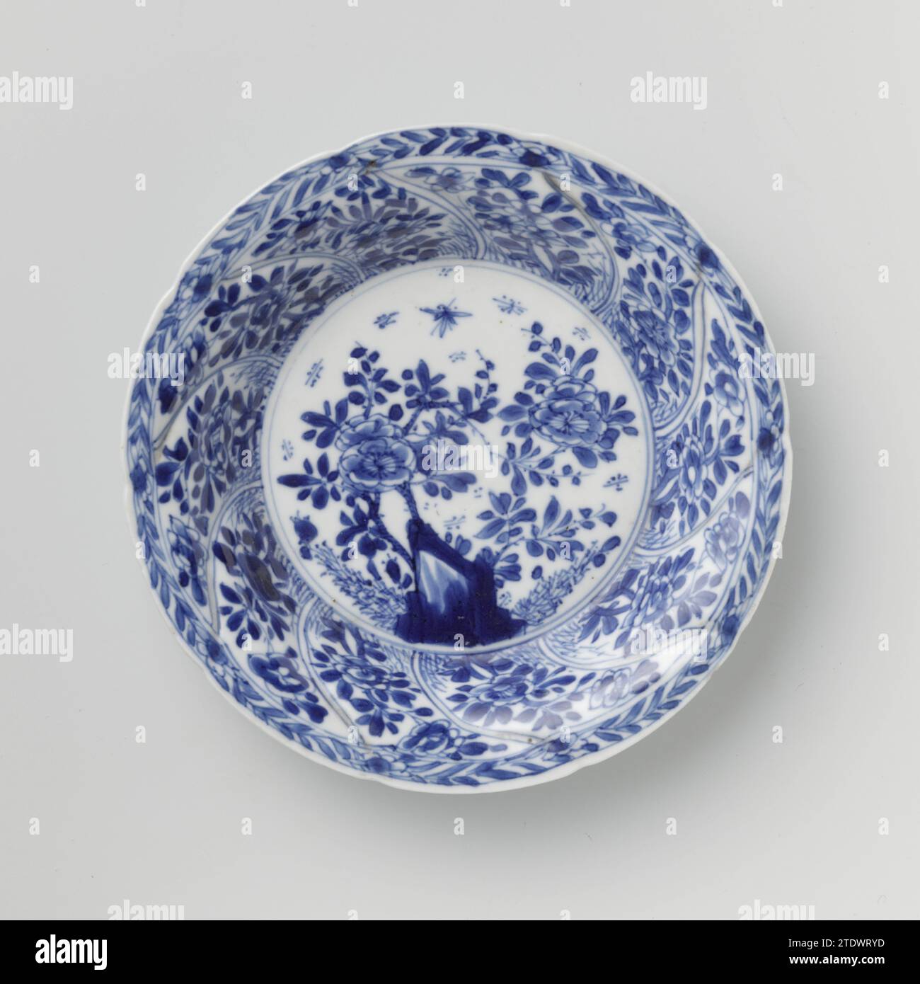 Soucoupe avec panneaux torsadés et sprays de fleurs, anonyme, c. 1680 - c. 1720 soucoupe en porcelaine avec mur rond modelé en dix cours torsadés, peinte en bleu sous-couche. Sur le plat un rocher avec une branche de fleur, des plantes et un papillon ; Une branche de fleur sur le mur dans chaque boîte ; le bord avec une boisson de fleur ; sur le dos aussi une branche de fleur dans chaque boîte. Marqué sur la face inférieure du caractère chinois « Fú » dans un double cercle. Une puce dans le bord. Bleu blanc. Porcelaine de Chine. glaçage. Cobalt (minéral) peinture / vitrification soucoupe en porcelaine avec mur rond modelé en dix cours torsadés, peint en und Banque D'Images