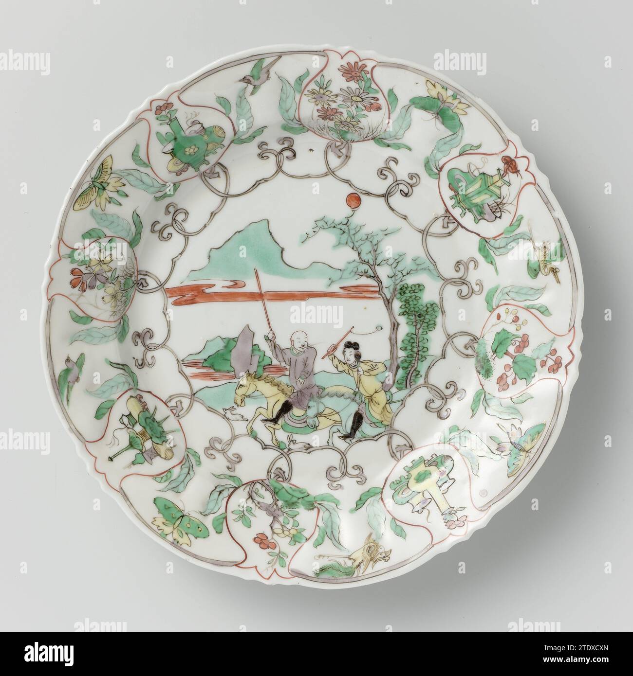 Plat festonné, anonyme, c. 1700 - c. 1724 plaque de porcelaine avec un bord festonné, peint sur le glaçage en rouge, vert, jaune, aubergine et noir. Sur le plat une scène de chasse avec deux cavaliers armés dans un paysage, chassant deux lièvres. Le mur et le bord avec une bande connectée de vignes de fleurs. Le bourgeon floral est toujours un cartouche avec des plantes à fleurs (aster, bel anjer) ou des antiquités (vase avec fleur ou champignon, brûleur d'encens, trépied). Parcourez et volez des oiseaux (grue, Feng Huang) ou des papillons entre les cartouches. Le bord extérieur avec deux branches de fleurs et une plante de lotus en fleurs. Mars Banque D'Images