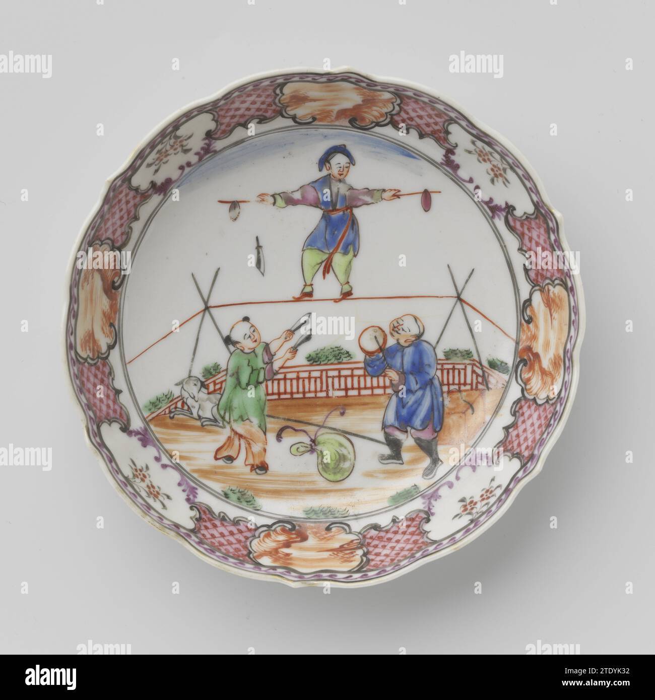 Soucoupe avec trois acrobates chinois et paysages en panneaux, anonyme, c. 1775 - c. 1799 plat en porcelaine avec paroi droite, nervurée et bord festonné, peint sur la glaçure en bleu, rouge, rose, vert, noir et or. Sur le plat du plat trois acrobates chinois dans un jardin clôturé, dont l'un est sur la corde faible, le deuxième jeune avec des couteaux et le dernier avec une plaque tournante sur un bâton ; Un chien horizontal à côté d'eux, au premier plan un sac noué; le mur avec servetwork entrecoupé de cartouches avec des paysages ou des branches de fleurs. Une fissure dans le fond. Rose de famille/mandarine. Porcelaine Banque D'Images