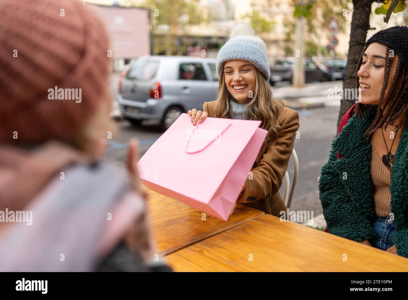 Trois femmes partagent des rires autour d'une boisson chaude dans un café en plein air, mettant en valeur un style de vie urbain détendu. Banque D'Images