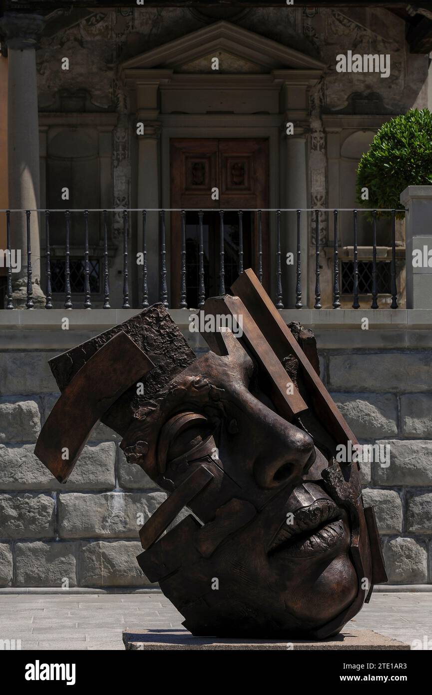 Sculpture d'une énorme tête humaine par l'artiste polonais Igor Mitoraj (1944 - 2014), sur la Piazza Mino da Fiesole, la place principale de Fiesole, une ville au-dessus de Florence, Toscane, Italie. En arrière-plan se trouve le portique ionique de la Chiesa di Santa Maria Primerana, qui a été ajouté à cette église médiévale en 1801. La façade de l’église date de la fin des années 1500 Banque D'Images