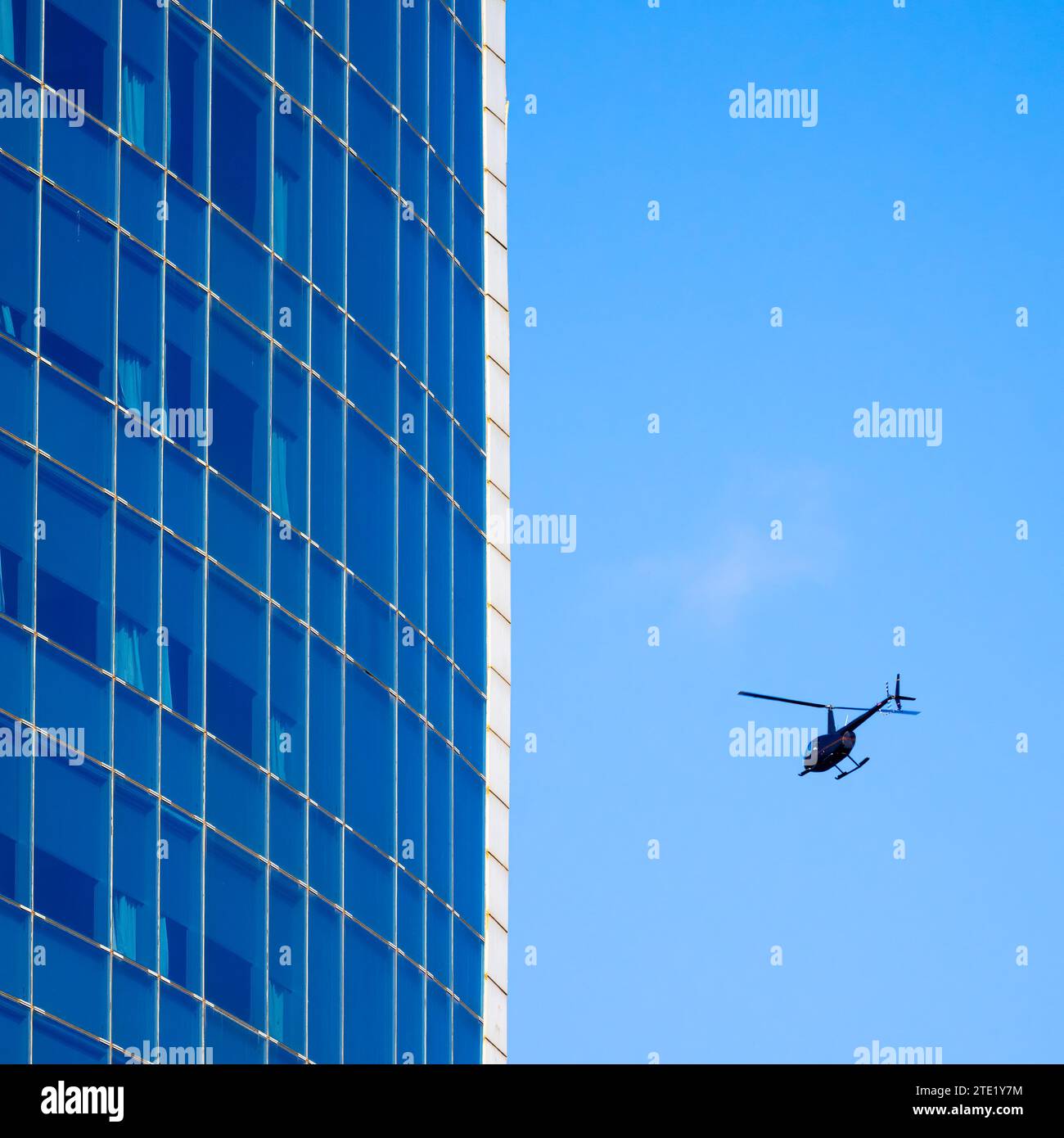 Un hélicoptère survole un grand gratte-ciel bleu à Barcelone, en Espagne Banque D'Images
