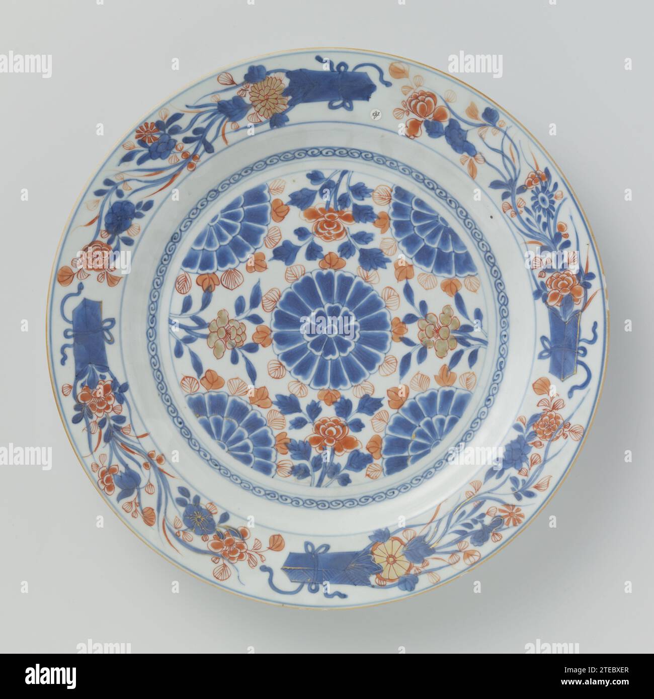 Plat avec des têtes de fleurs stylisées, sprays de fleurs et bouquets, anonyme, c. 1700 - c. 1724 soucoupe en porcelaine, peinte en bleu glacé et sur le glaçage rouge et or. Sur le plat un médaillon avec une fleur stylisée au centre et des fleurs à moitié stylisées sur les bords, ici entre les branches de fleurs ; autour du médaillon une bande avec un travail de boucle ; quatre bouquets avec des fleurs fleuries sur le bord ; le dos avec trois branches de fleurs. Imari chinois. Porcelaine de Chine. glaçage. cobalt (minéral). Or (métal) peinture / dorure / vitrification soucoupe en porcelaine, peinte en bleu glacé et sur la glaçure Banque D'Images