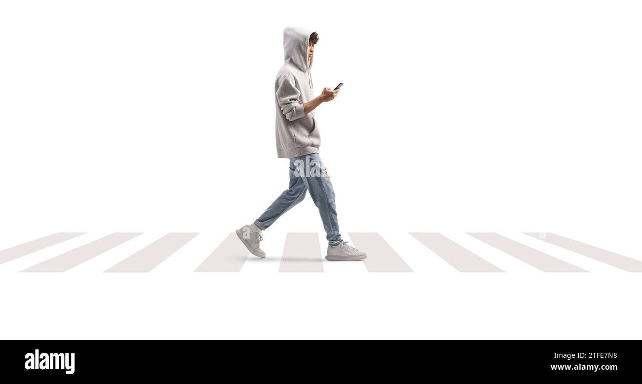 Photo en longueur d'un gars portant un sweat à capuche gris et marchant avec un smartphone à un passage piéton isolé sur fond blanc Banque D'Images