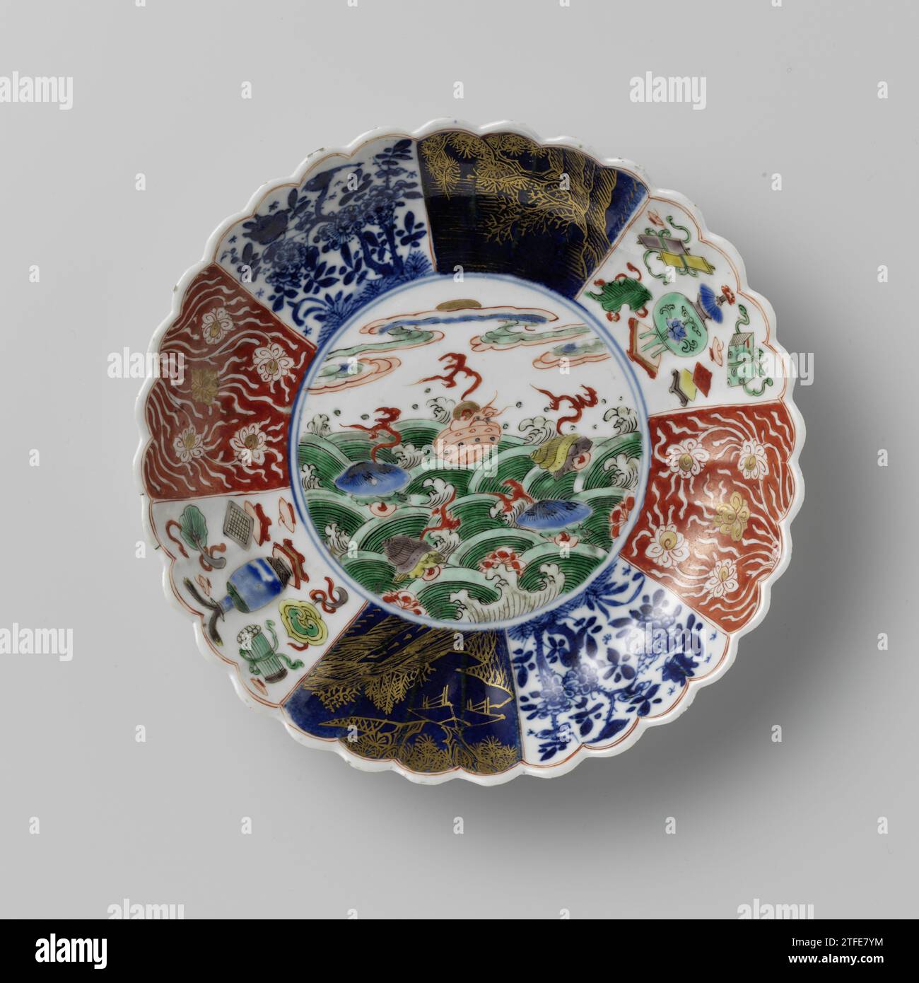 Soucoupe-plat avec côtés cannelés et fleurs et crustacés au-dessus des vagues, anonyme, c. 1700 - c. 1724 bol en porcelaine avec paroi nervurée et bord lobé, peint en bleu sous glaçure et sur le glaçage bleu, rouge, vert, jaune, aubergine, noir et or. Sur le plat un médaillon avec des fleurs de prunus et des crustacés au-dessus des vagues tourbillonnantes ; le mur divisé en huit cours avec la même décoration de l'autre côté: Lotus vrilanks sauvé contre un sol rouge, arbres fleuris avec oiseau et papillon, un paysage en or contre un bleu poudré (bleu poudré) sol et coûteux (Artemisiablad) avec des symboles chanceux (trois - Banque D'Images