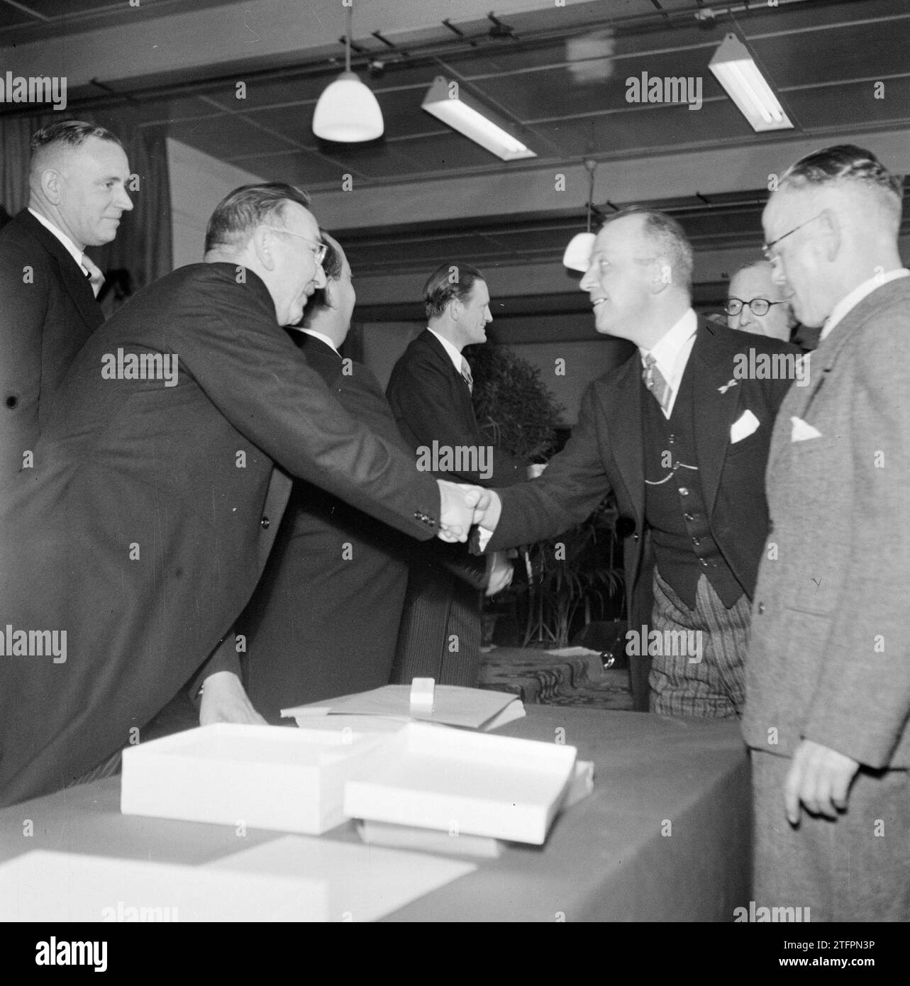 Groupe d'hommes autour d'une table, dont deux se serrent la main ; droite maire Kolfschoten, de retour dans le profil directeur de l'usine Albert van Abbe, 3e à partir de la gauche (seulement partiellement visible) son frère et co-directeur Jan van Abbe ca. 1950 Banque D'Images