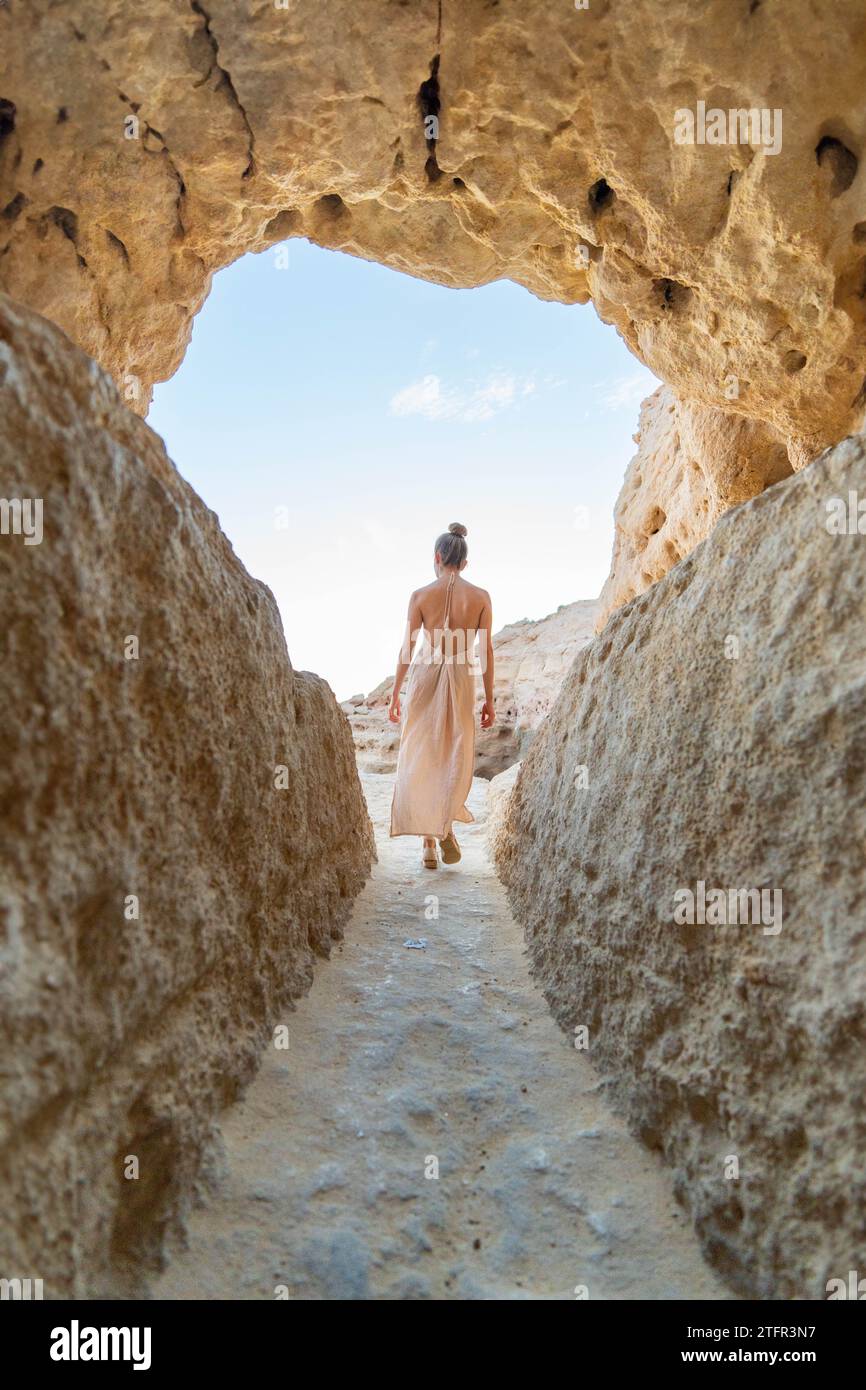 Voyage à travers l'arche naturelle : un petit angle, prise de vue verticale d'une femme dans une robe fluide, s'éloignant de la caméra Banque D'Images