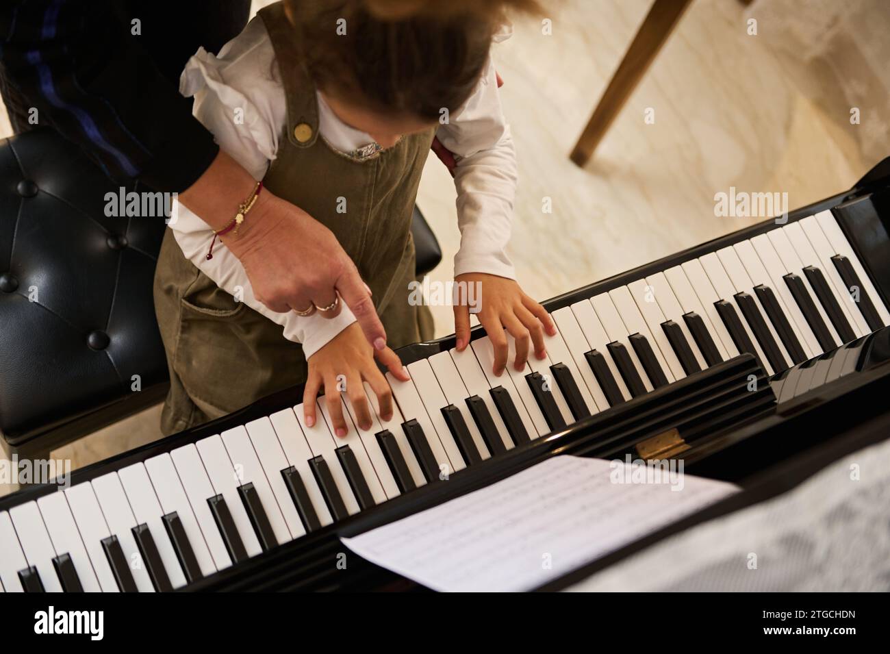 Vue de dessus en gros plan de la main de l'enfant avec les doigts touchant les touches du piano sous la direction d'un professeur de pianiste musicien expliquant la leçon de piano Banque D'Images