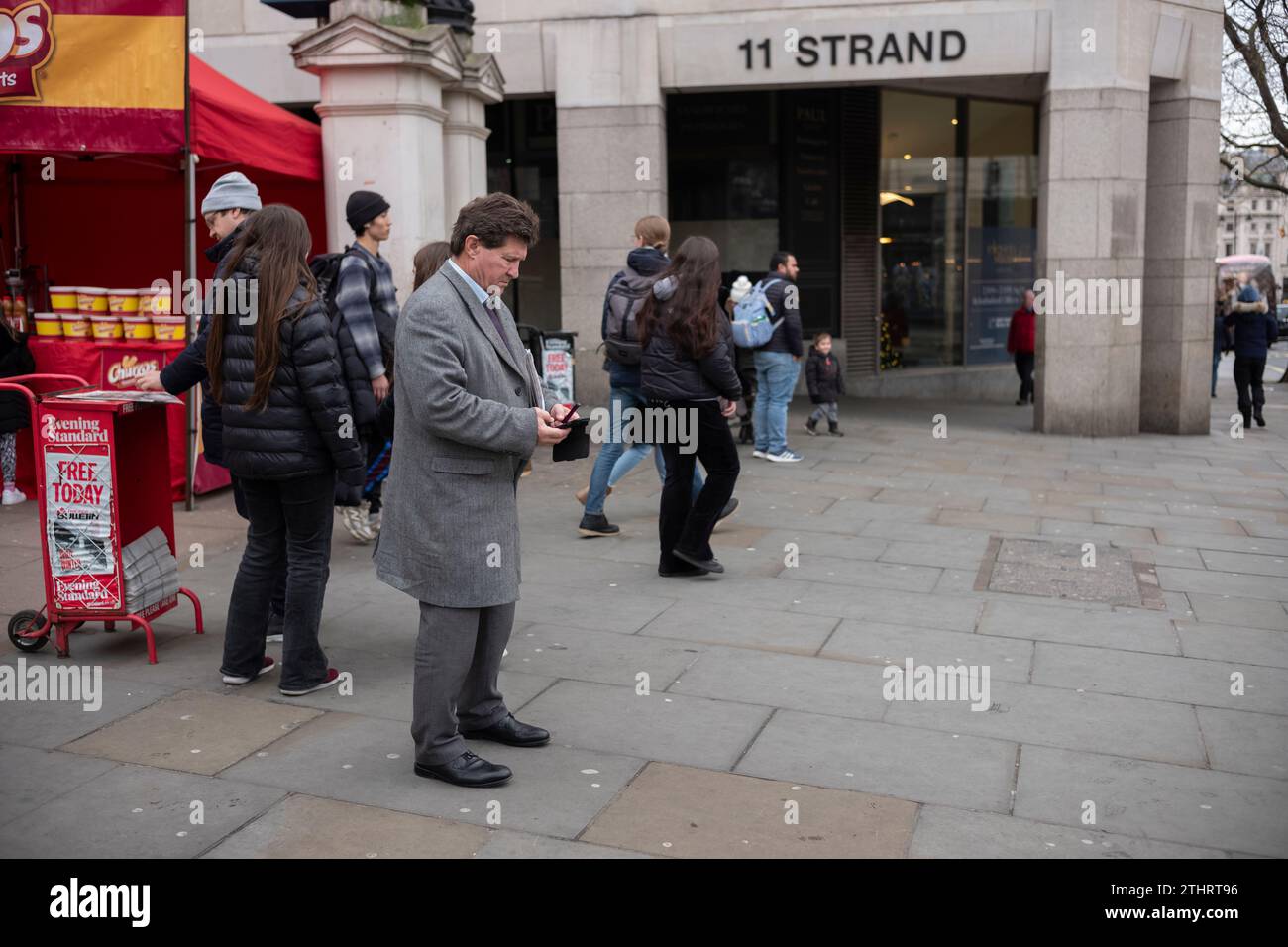Un homme d'affaires vérifie son téléphone alors qu'il se tenait sur le Strand à l'extérieur de la gare de Charing Cross, au cœur du West End de Londres. Banque D'Images
