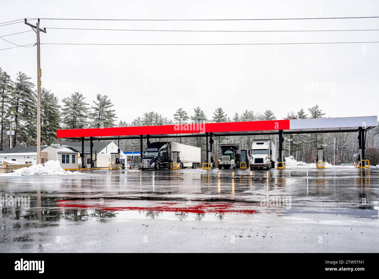 Les gros camions semi-remorques avec semi-remorques ravitaillent les réservoirs à une station-service sur un parking d'arrêt de camion d'hiver avec de la neige et de la glace dans le New Hampshire, en Nouvelle-Angleterre Banque D'Images