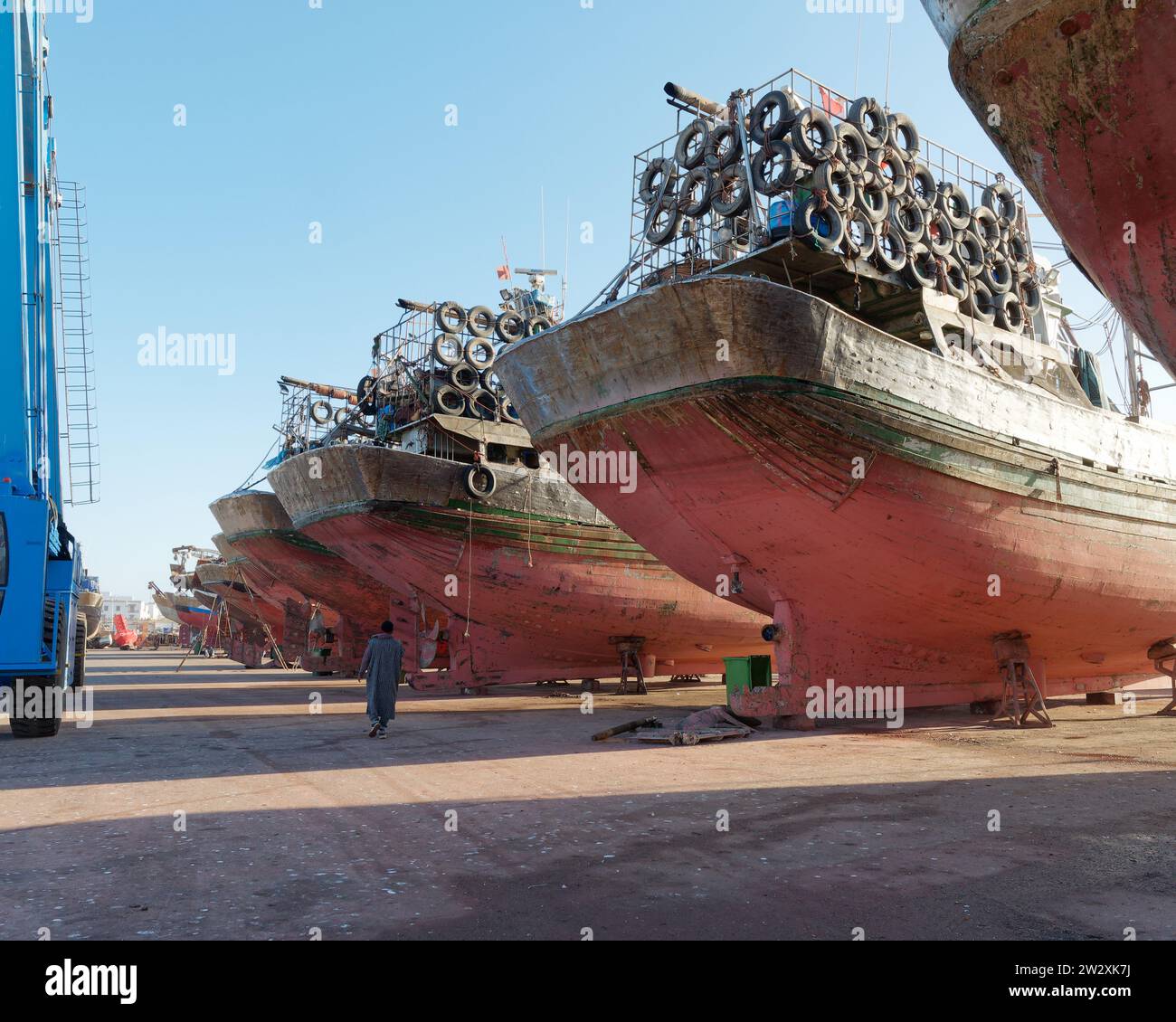 Un travailleur passe devant de grands navires et une grue à une cale sèche probablement pour l'entretien à Essaouira « la ville venteuse », au Maroc. 21 décembre 2023 Banque D'Images